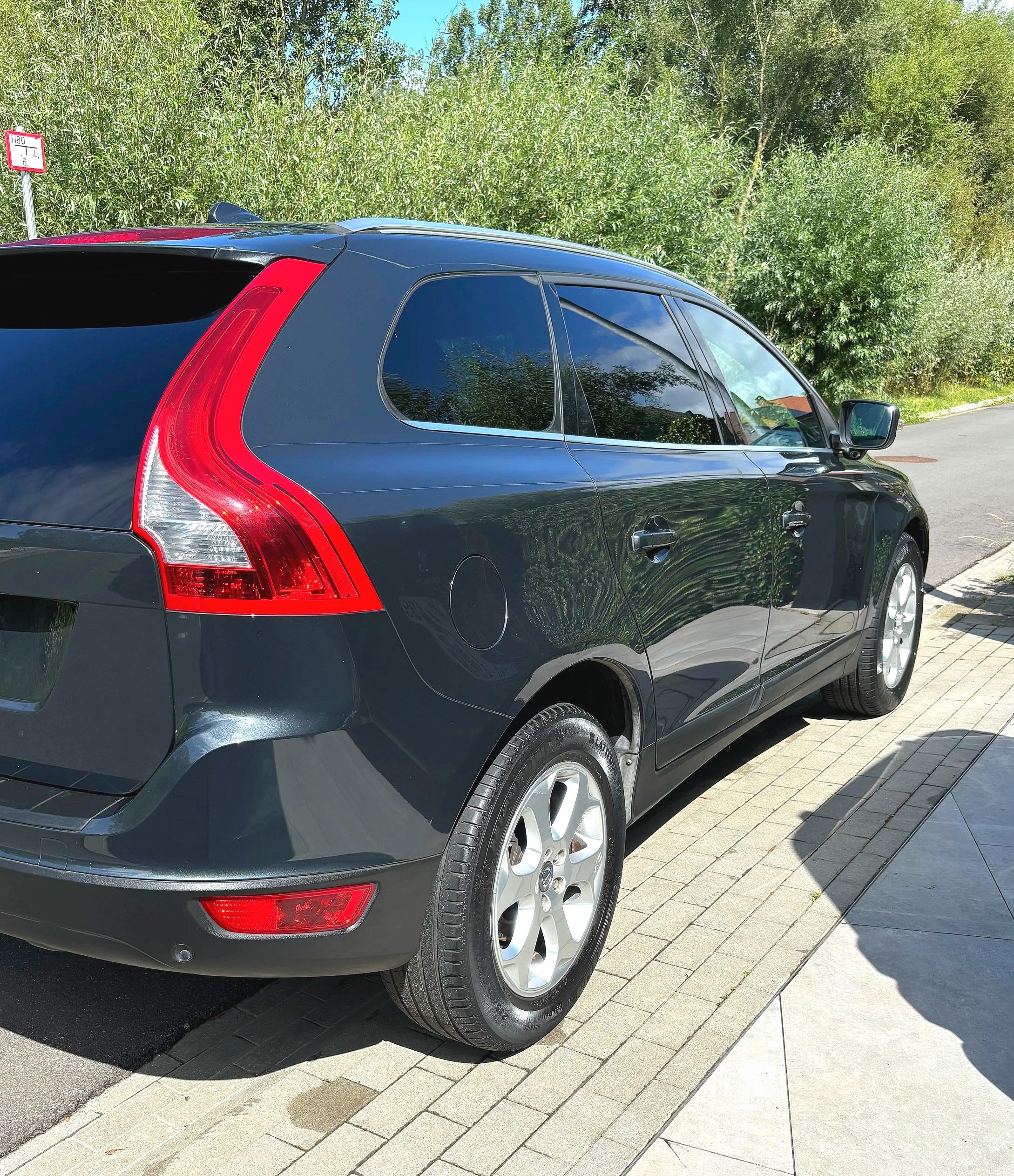 Zwarte stationwagen geparkeerd naast een trottoir, met groene struiken en bomen op de achtergrond.