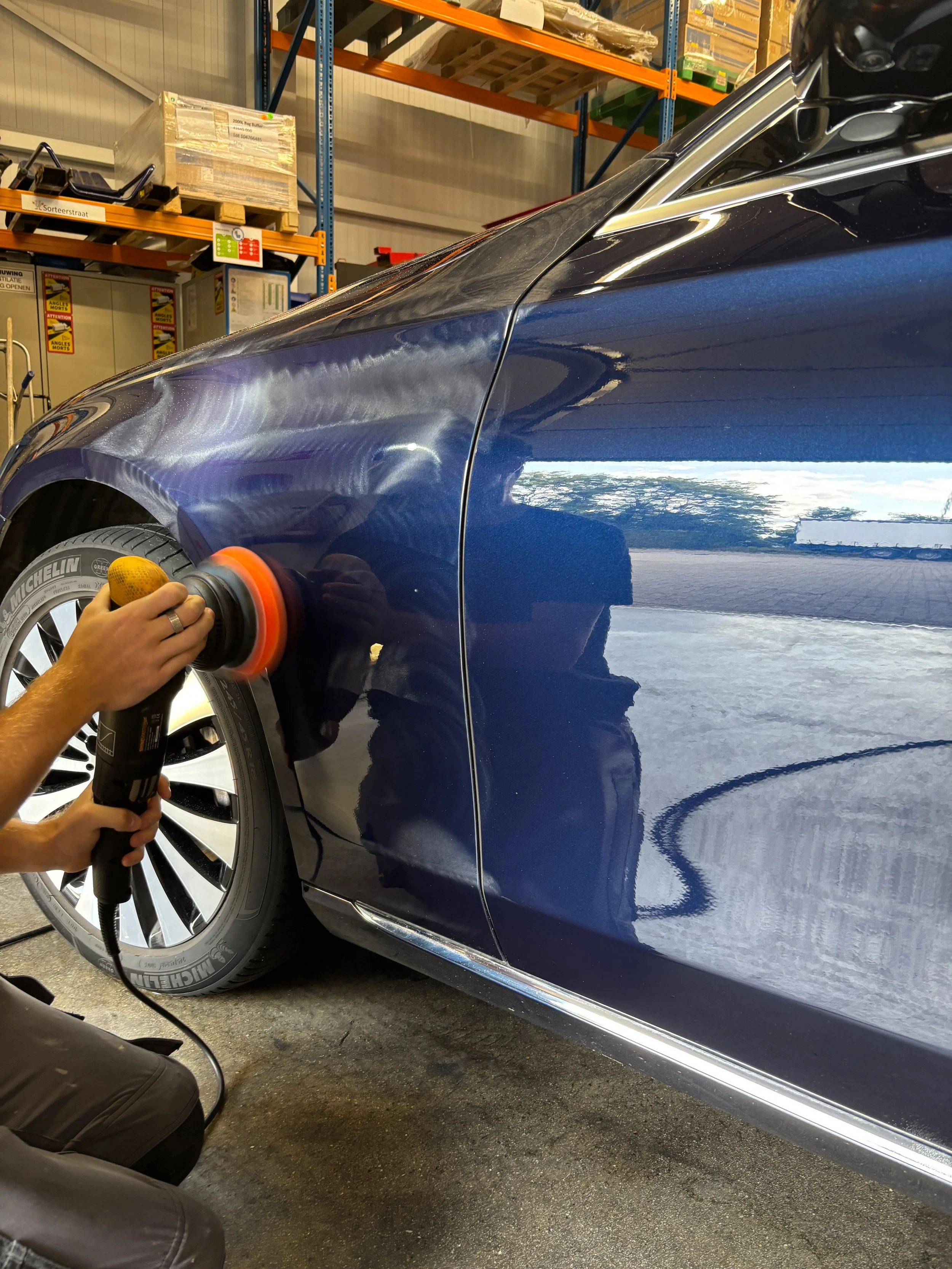 Persoon polijst een blauwe auto in een werkplaats.
