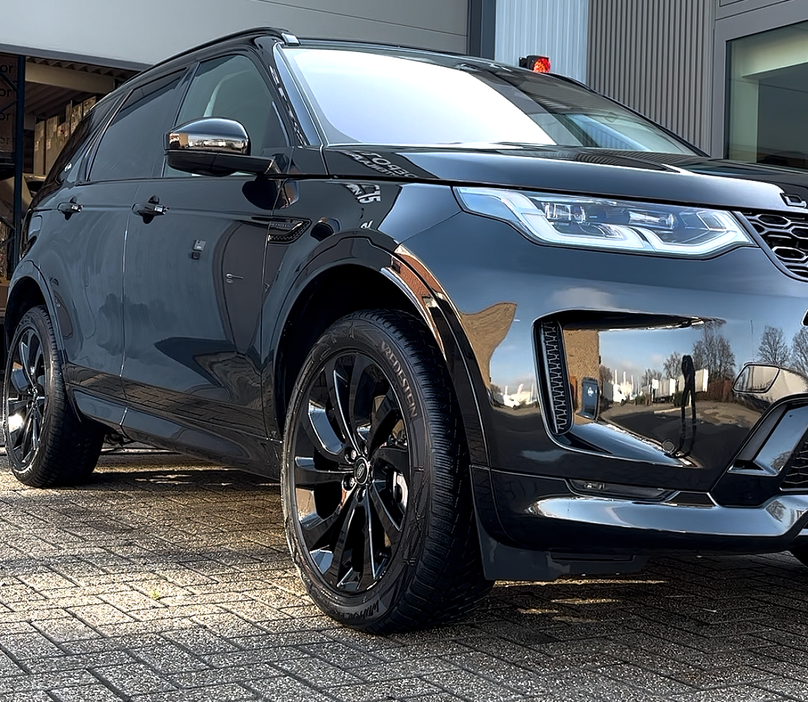 Een zwarte SUV geparkeerd op een grindachtige oprit, met de weerspiegeling van de omgeving zichtbaar op de carrosserie.