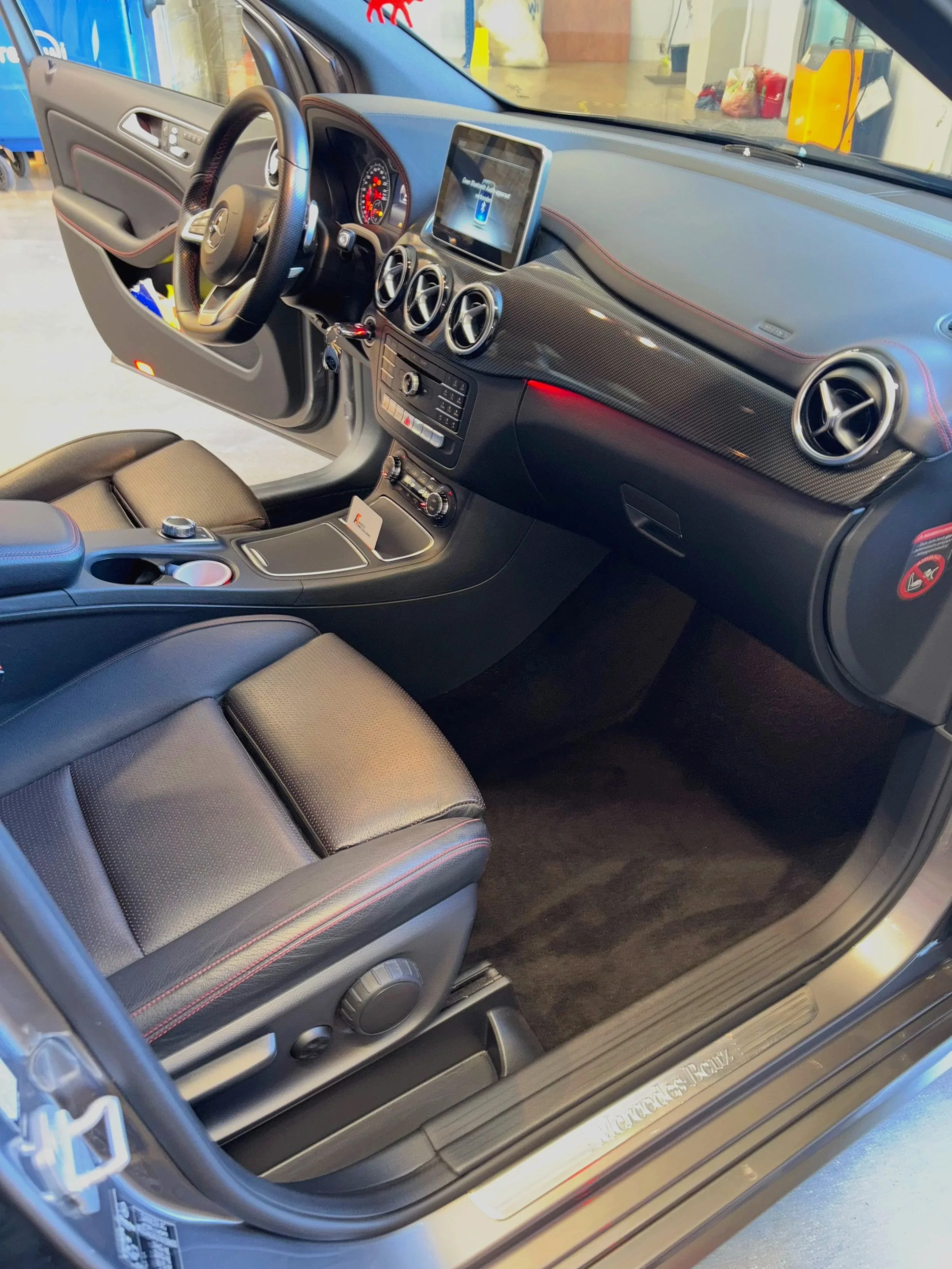 Interieur van een Mercedes-Benz sportauto, met een leren stuurwiel, drie ronde ventilatieopeningen, een digitaal display en een middenconsole met knoppen en een draaiknop.