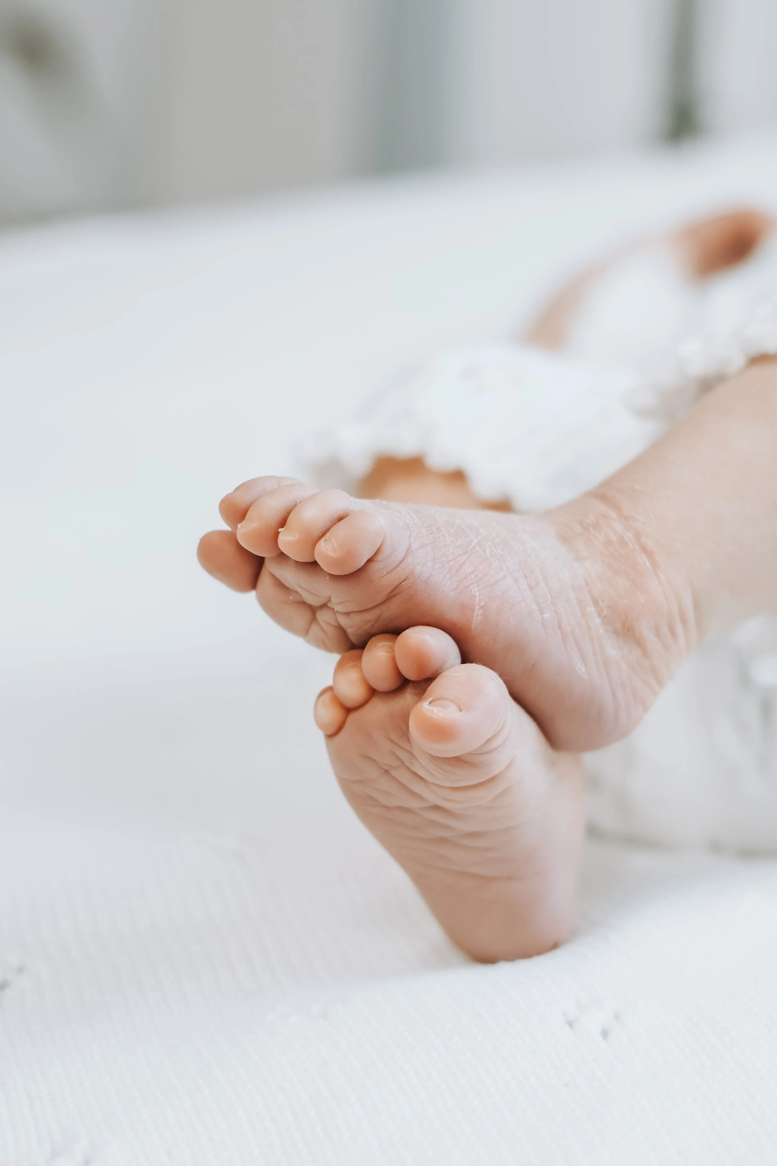 Close-up of a baby's hand and tiny foot resting on a white towel, with a blurred background.