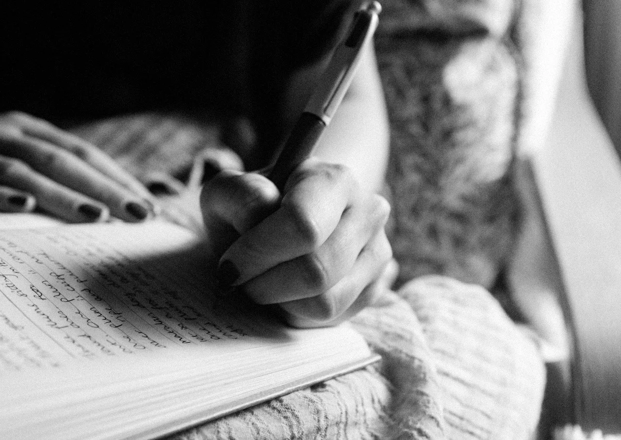 A person writing in a notebook with a pen, seen in black and white.