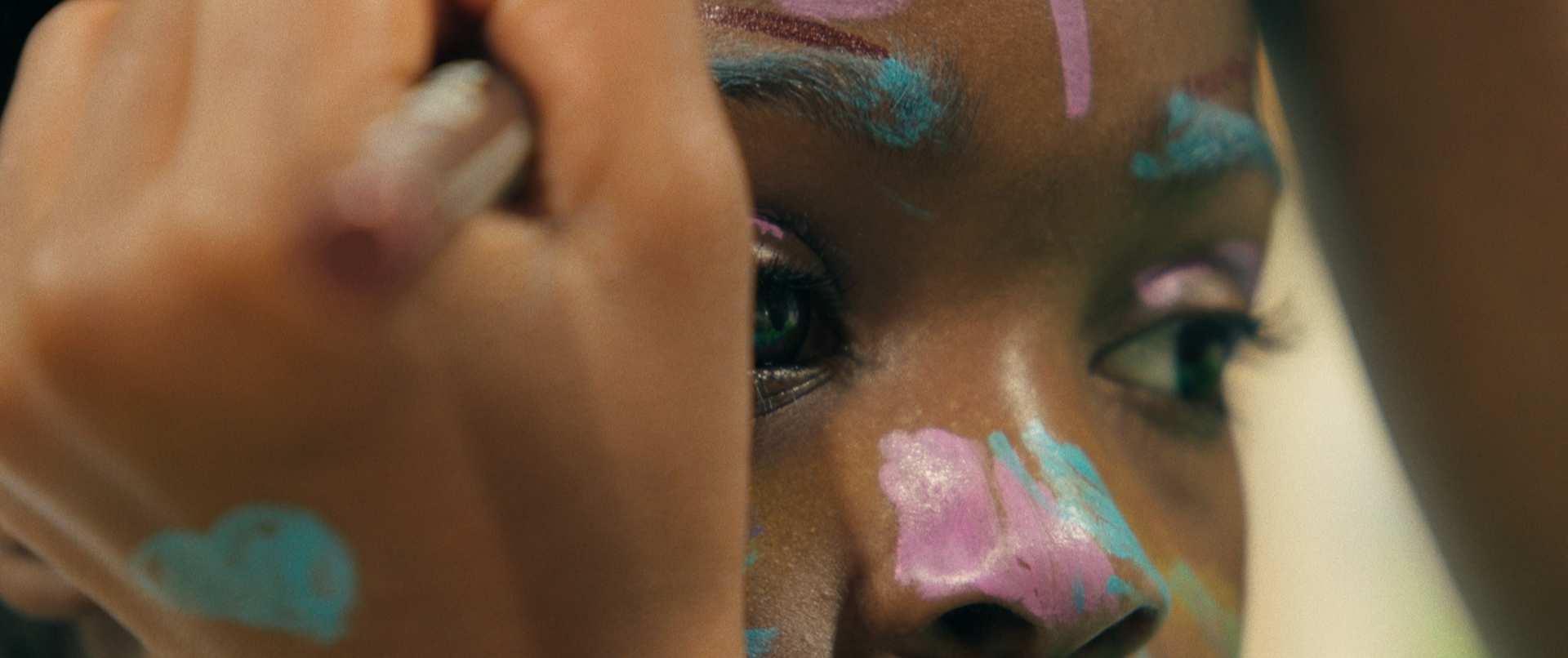 Close-up of a person's face with colorful face paint, looking into a mirror, applying makeup or face paint.