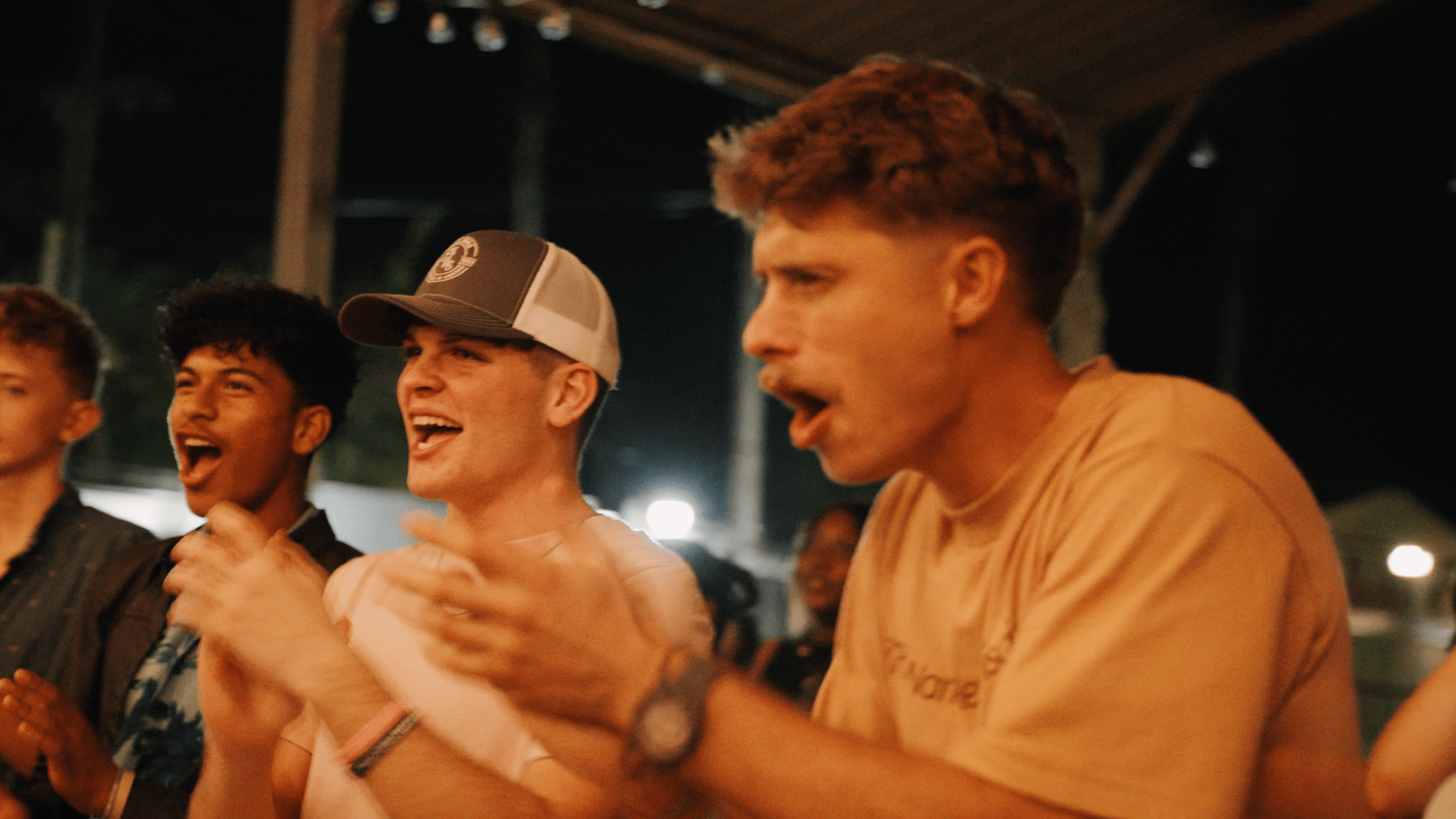 Group of young men laughing and clapping at night at an outdoor event.