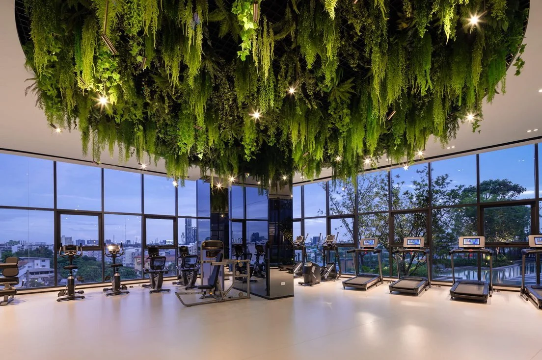 Modern gym at Ideo Sukhumvit-Rama 4 featuring full-height windows and lush green ceiling design with city views.