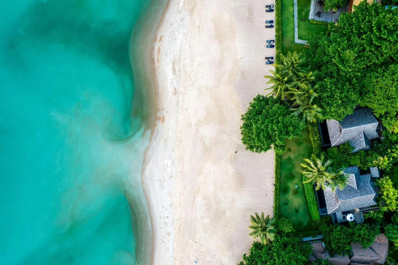Aerial view of Koh Samui coastline with clear turquoise water, sandy beach, and luxury beachfront villas surrounded by tropical greenery in Thailand.