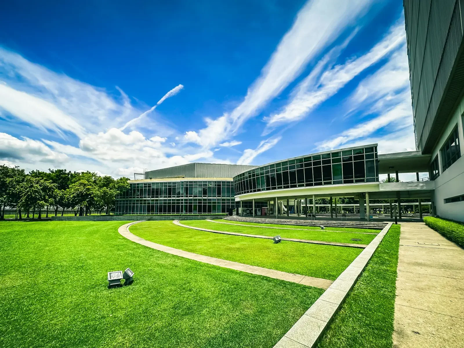 Bangkok international school campus with green lawn and glass-fronted buildings under blue skies.