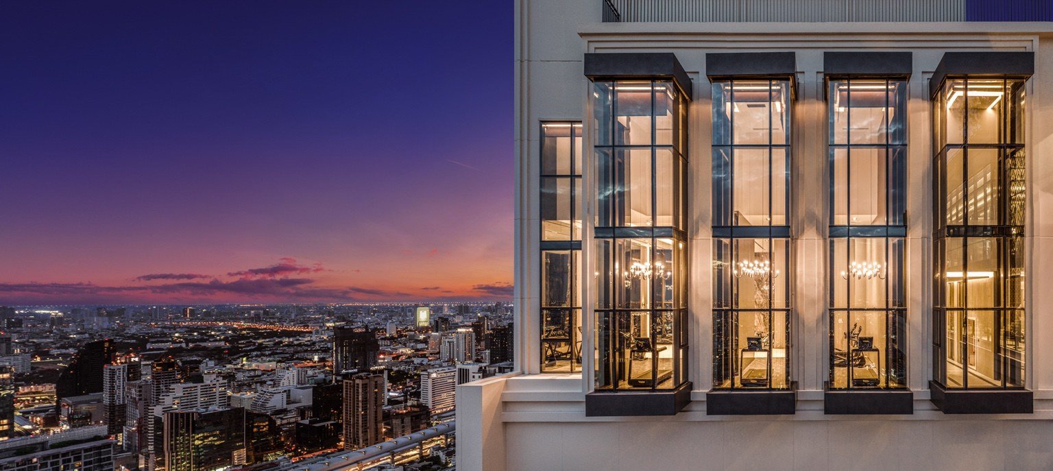 Upper façade at The Address Siam–Ratchathewi at dusk with floor-to-ceiling glazing and panoramic Bangkok skyline views.