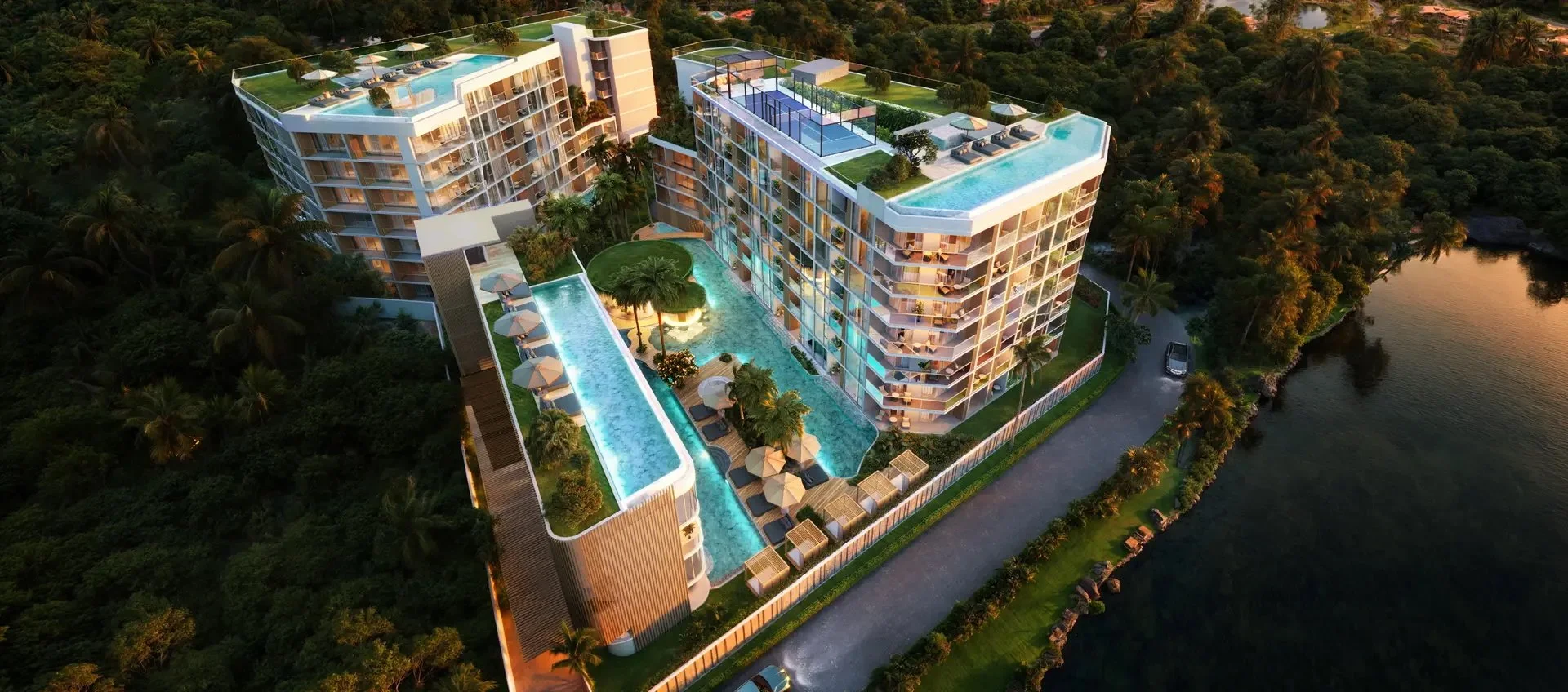 Aerial view of Siamese Bangtao at sunset, showing rooftop pools, central lagoon, and lush tropical surroundings in Phuket