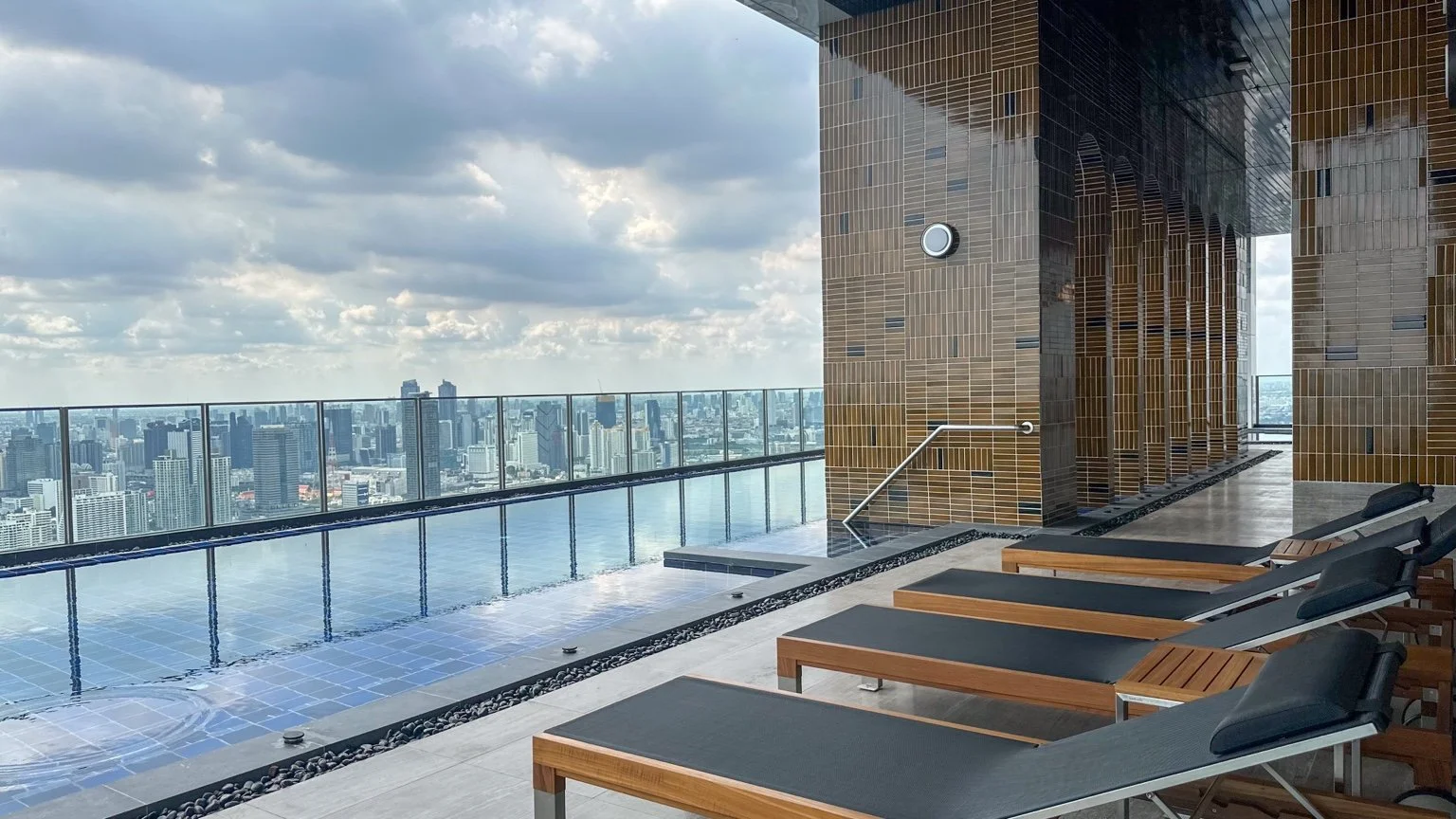 Sky lagoon pool deck at Noble Form Thonglor with sun loungers and city skyline views.