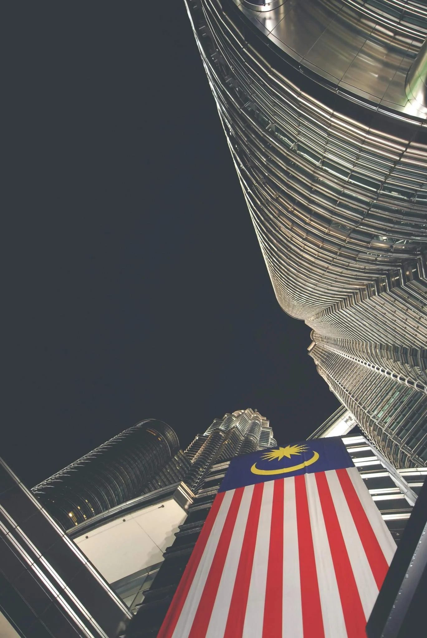 Malaysian flag draped from Kuala Lumpur Petronas Towers at night.