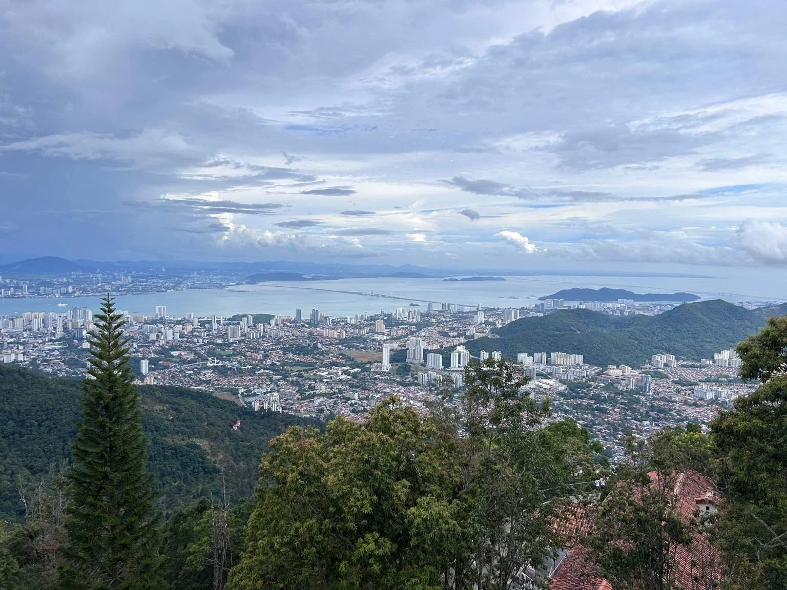 Panoramic view from Penang Hill overlooking George Town, the Penang coastline and the Strait of Malacca, with forested hills in the foreground.