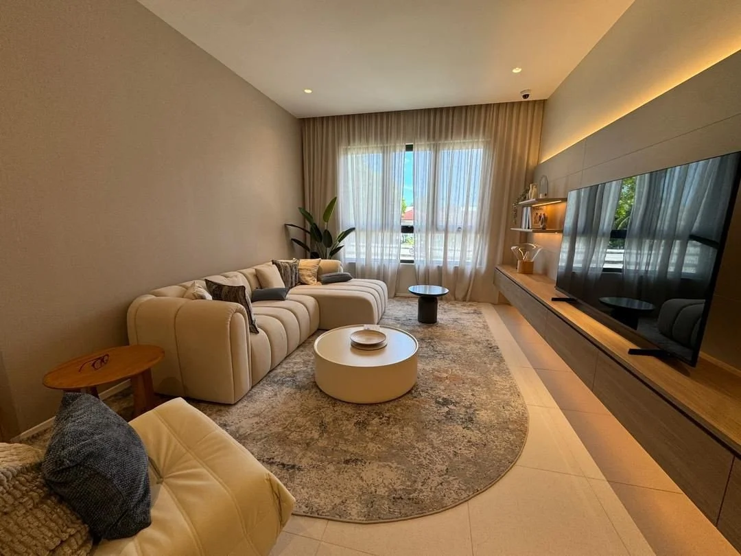 Waterstone Penang show unit living room with modern sofa seating, built-in TV wall and soft natural light from full-height windows.