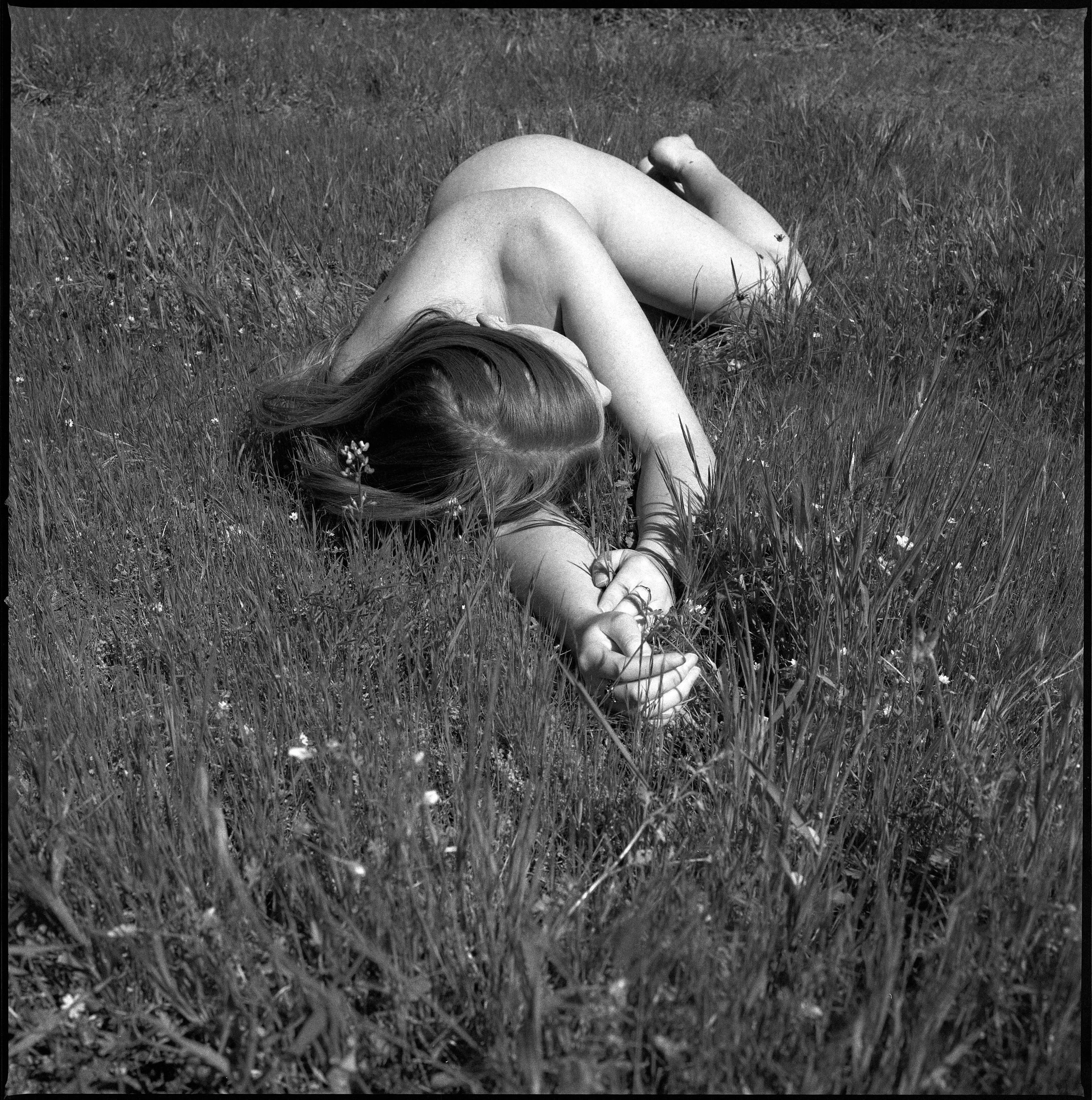 Nude model laying out in a field of grass in the sunshine in California photographed with a Hasselblad 500c/m and Ilford HP5 black and white film.