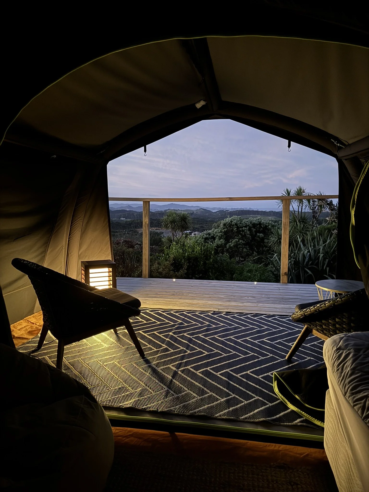 A person relaxing outside of a white tent, surrounded by greenery and bushes, under a clear sky. Bluewater Sanctuary Tutukaka