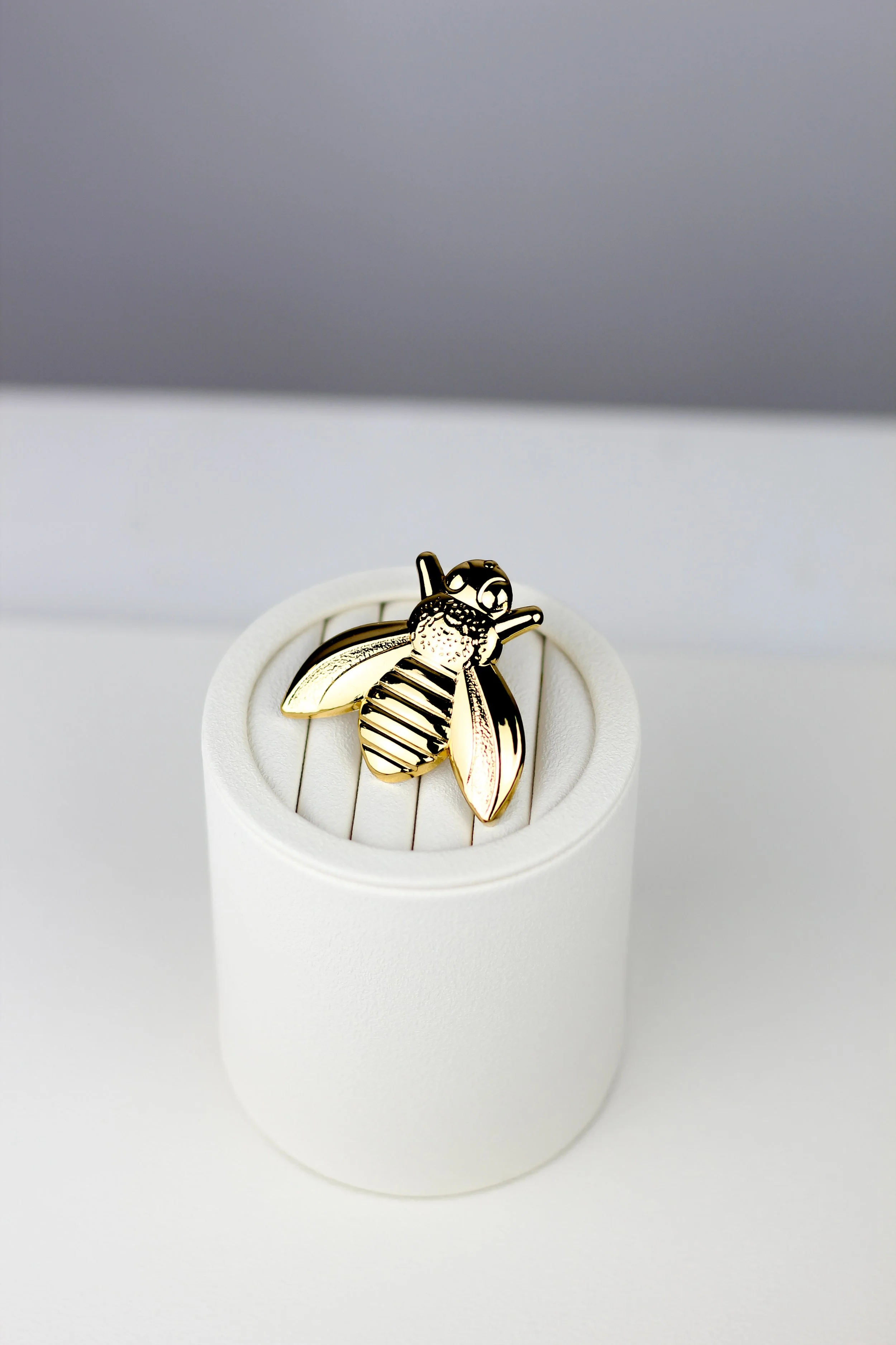 Gold bee-shaped ring displayed on a white stand.