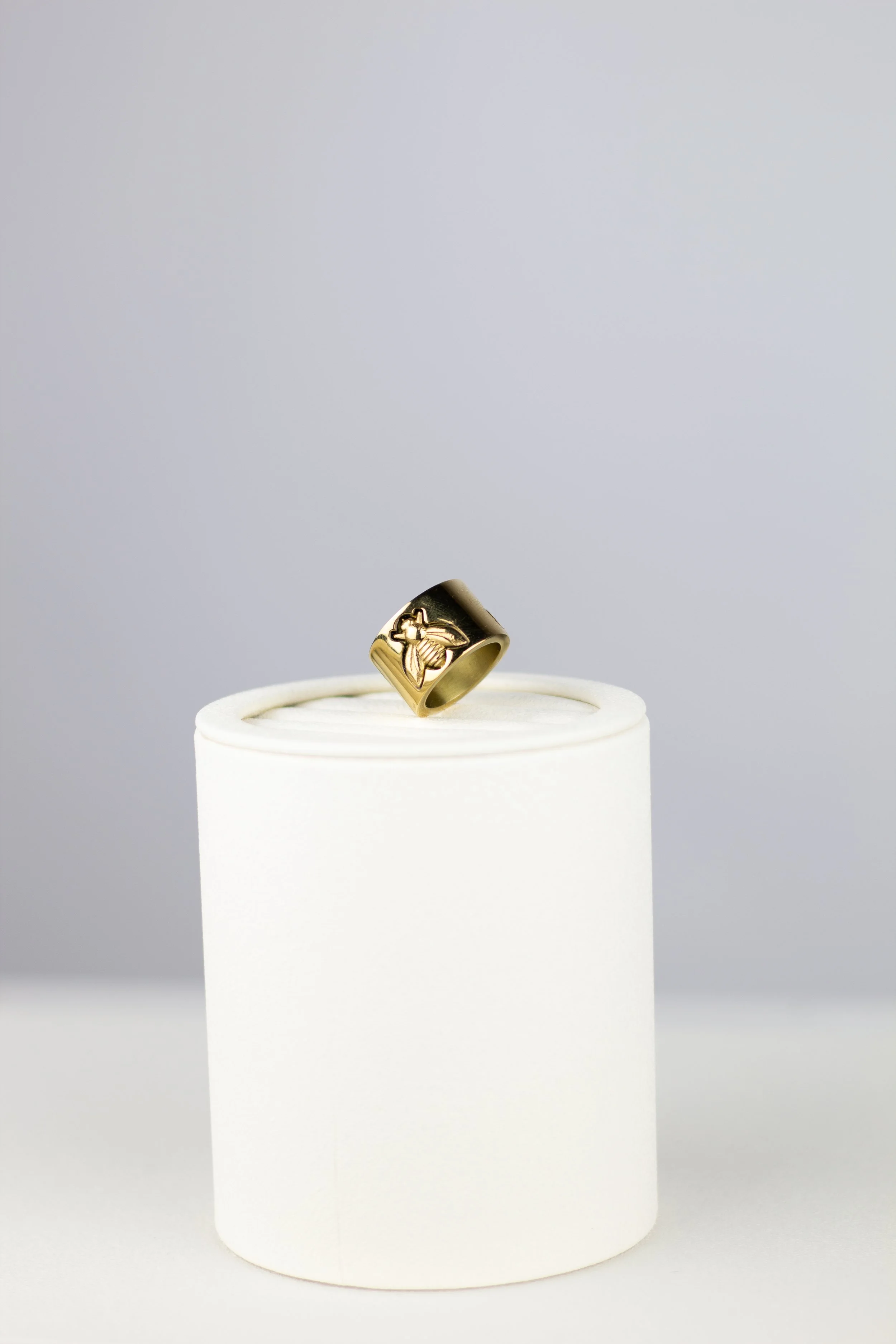 Gold ring with a hummingbird design on a white display stand against a light gray background.