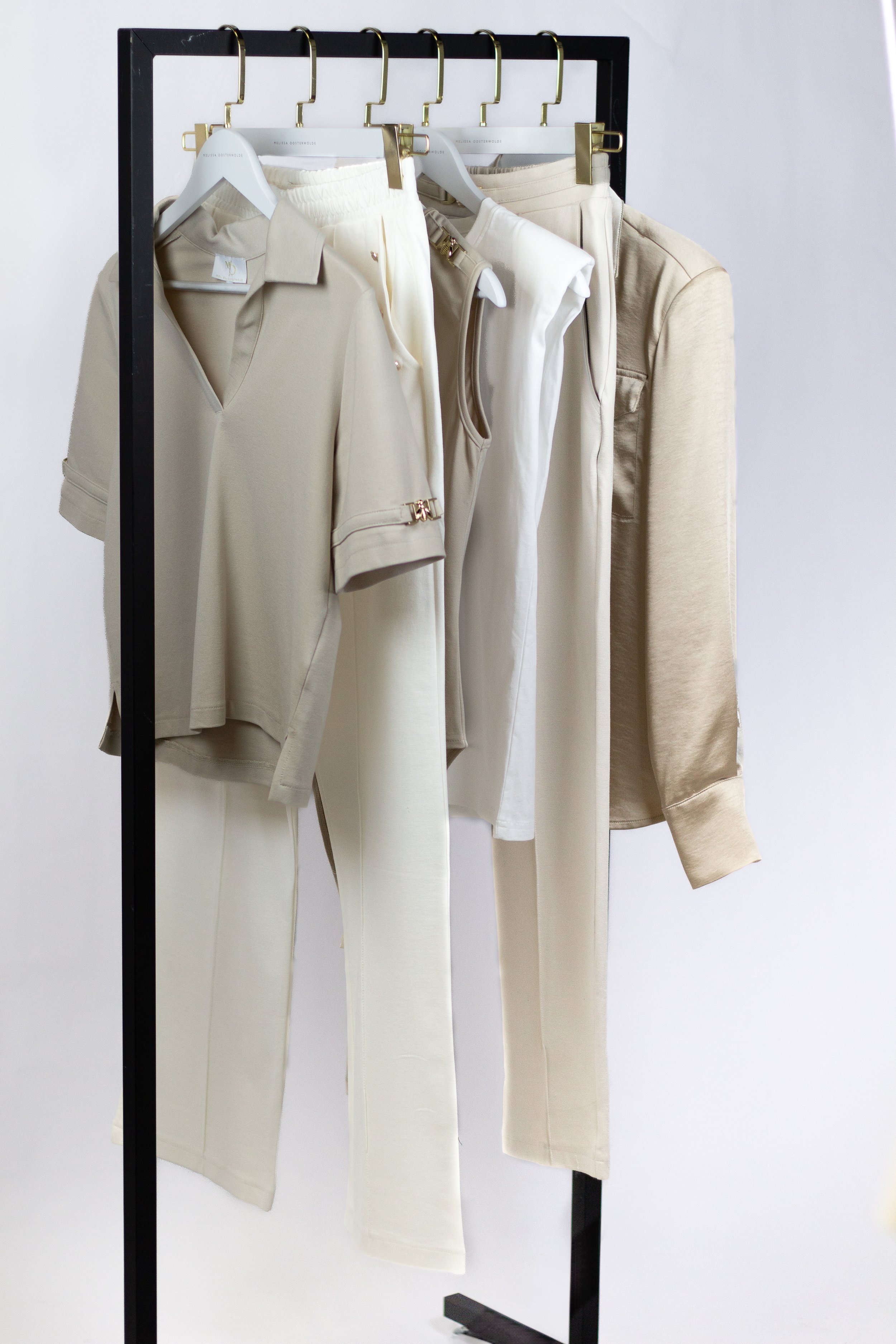 A clothing rack displaying beige, white, and neutral-colored casual outfits and loungewear, including shirts, pants, and hoodies.