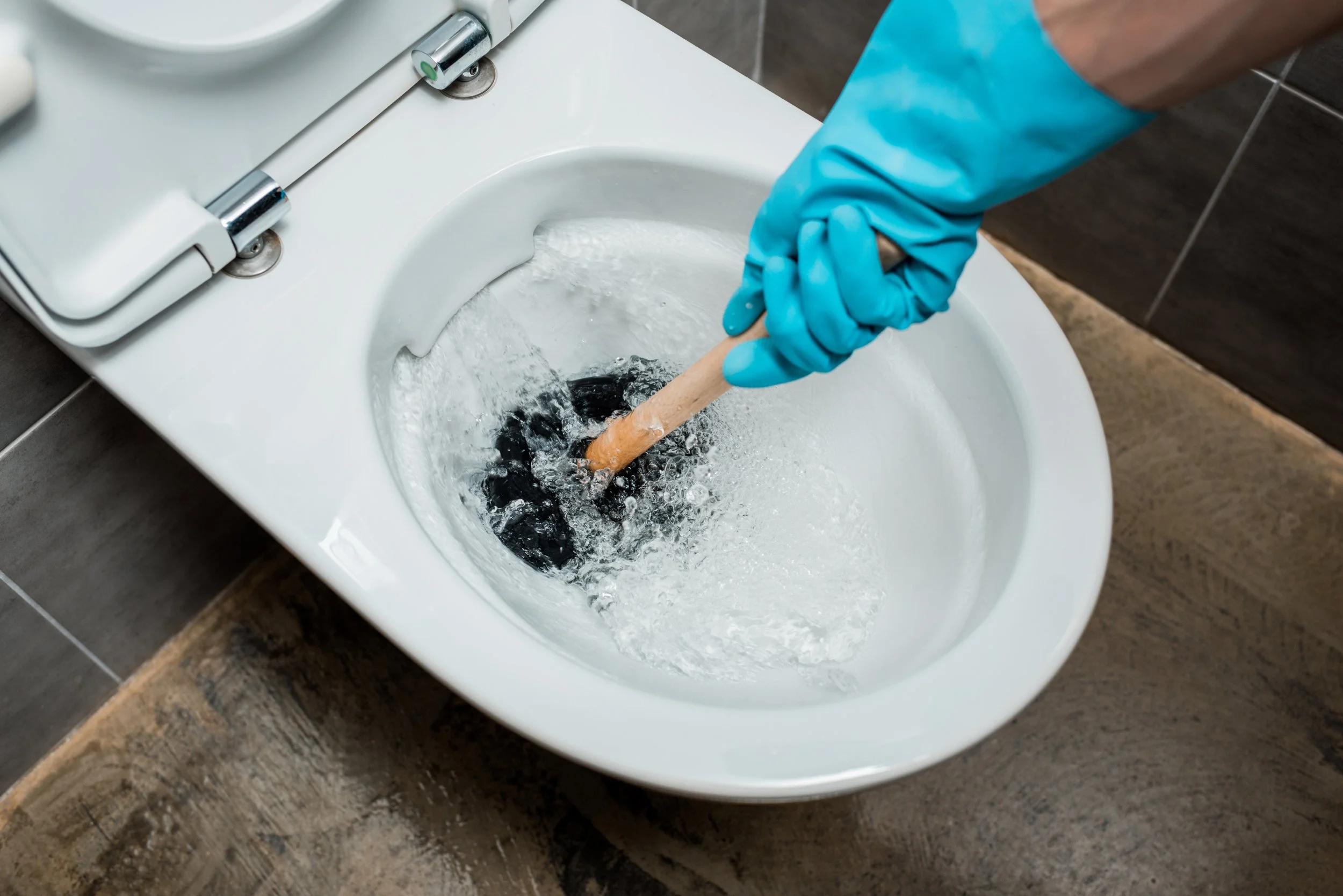 Person wearing blue gloves using a plunger to unclog a toilet.