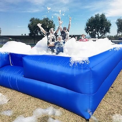 People playing in a large outdoor foam pit with blue inflatable walls.