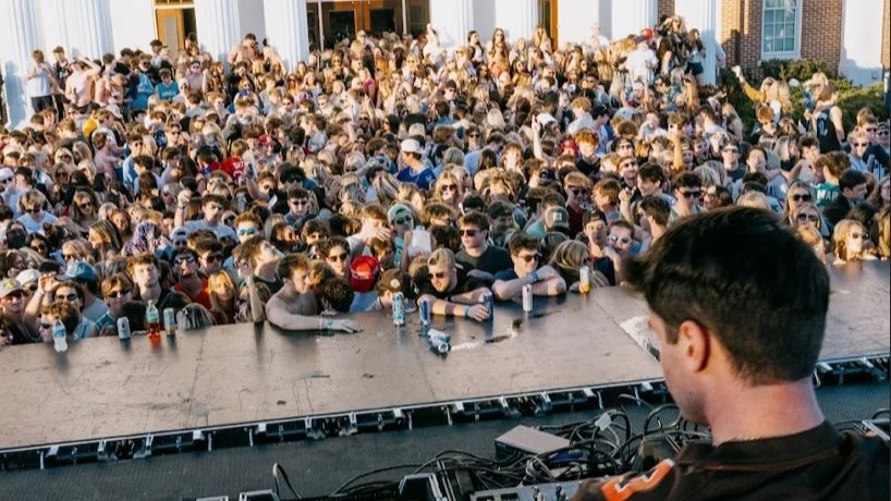 DJ performing at outdoor concert with large crowd in daylight