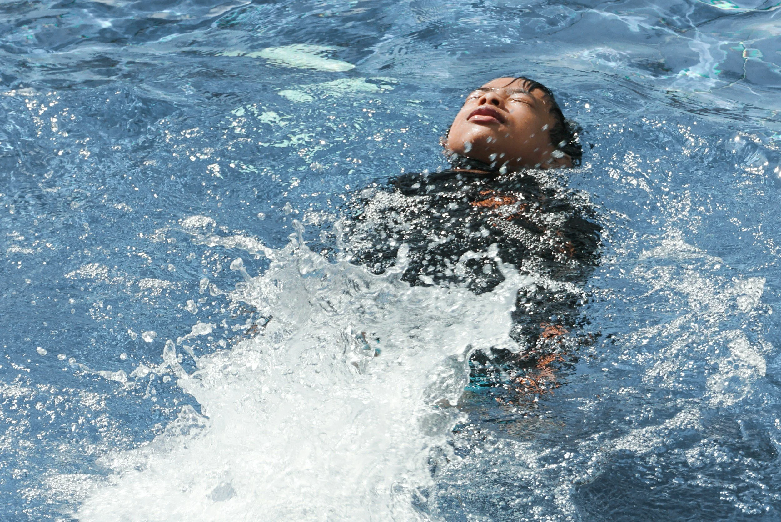 A person floating on their back in a swimming pool with eyes closed and a relaxed expression.