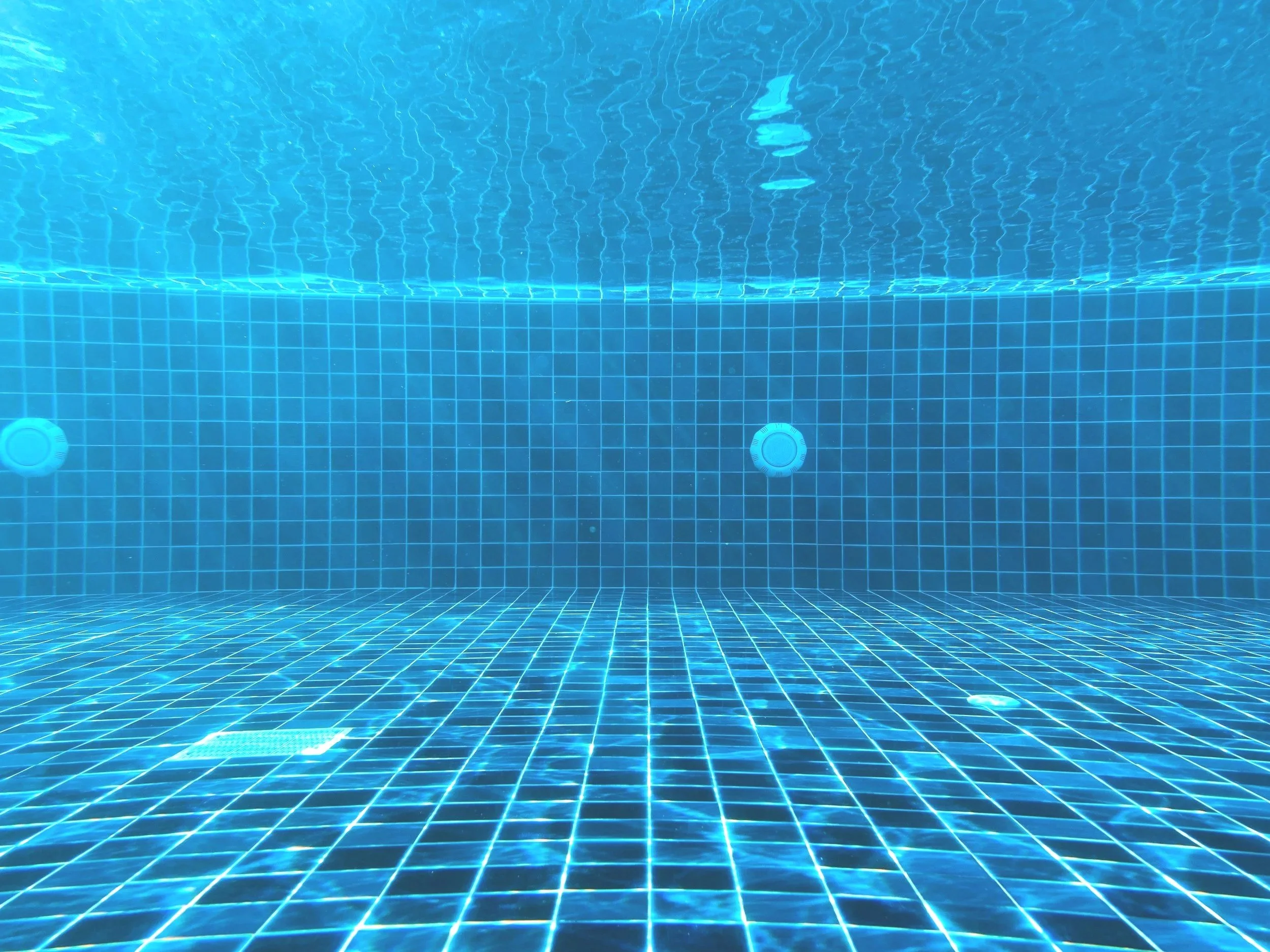 A vibrant blue swimming pool with steps, surrounded by a tiled edge, under a clear sky.