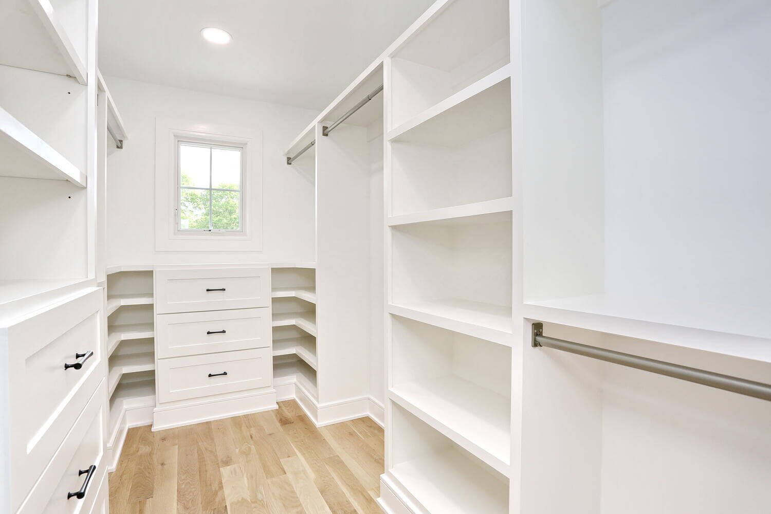 Bright primary closet with window, built-in drawers, and white cabinetry in a modern farmhouse by Dadak LLC, Park Ridge NJ.