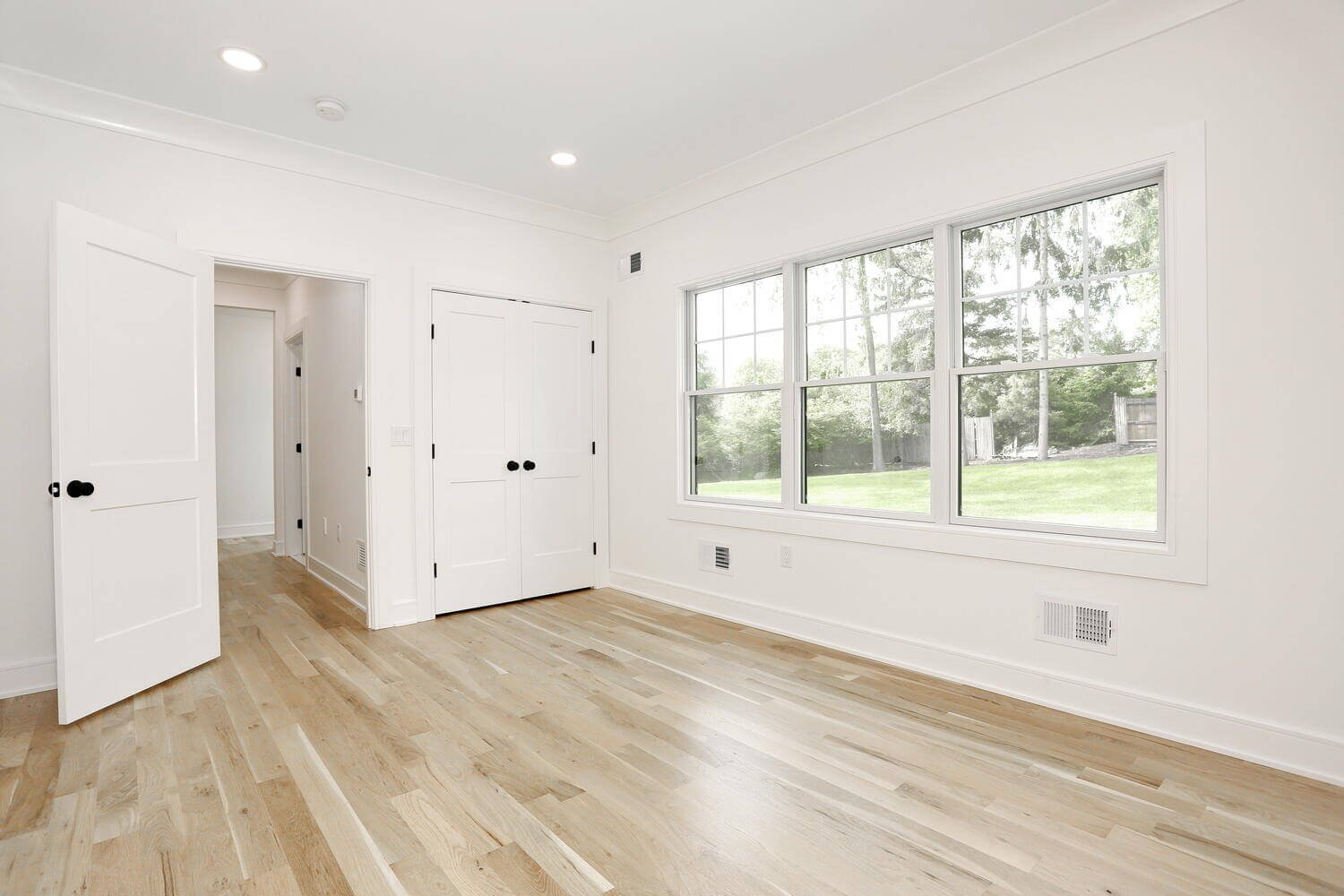 Spacious bedroom with large window, double closet doors, and light hardwood floors in a Park Ridge modern farmhouse by Dadak LLC.