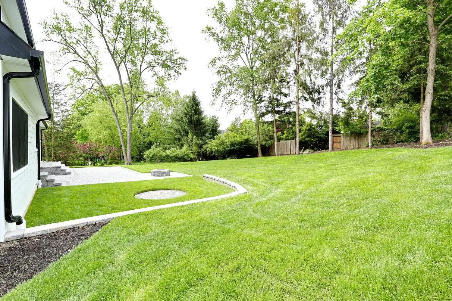 Expansive backyard with lush green lawn, mature trees, and paver patio in a Park Ridge modern farmhouse by Dadak LLC.