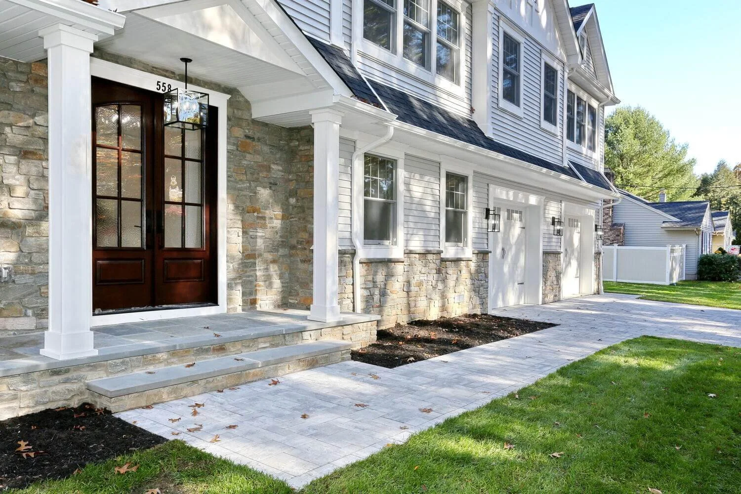 Front entryway of a custom home by Dadak LLC in River Vale, NJ featuring stone façade, dark wood double doors, and white trim columns — modern Bergen County home exterior.