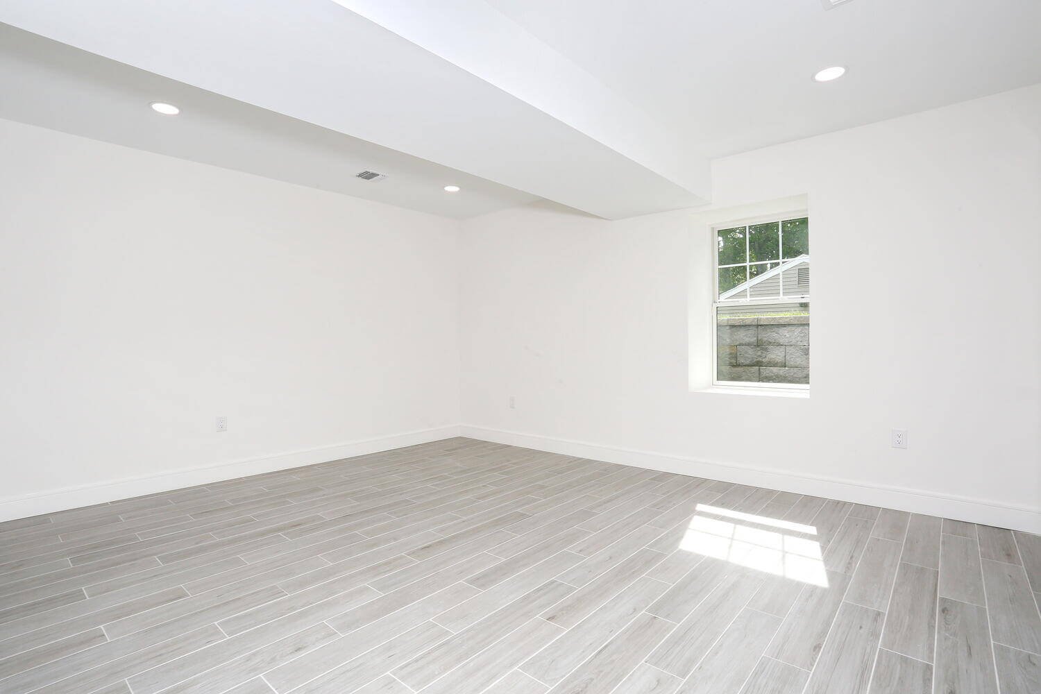Lower level bedroom with a large window and light gray tile flooring in a Park Ridge modern farmhouse by Dadak LLC.
