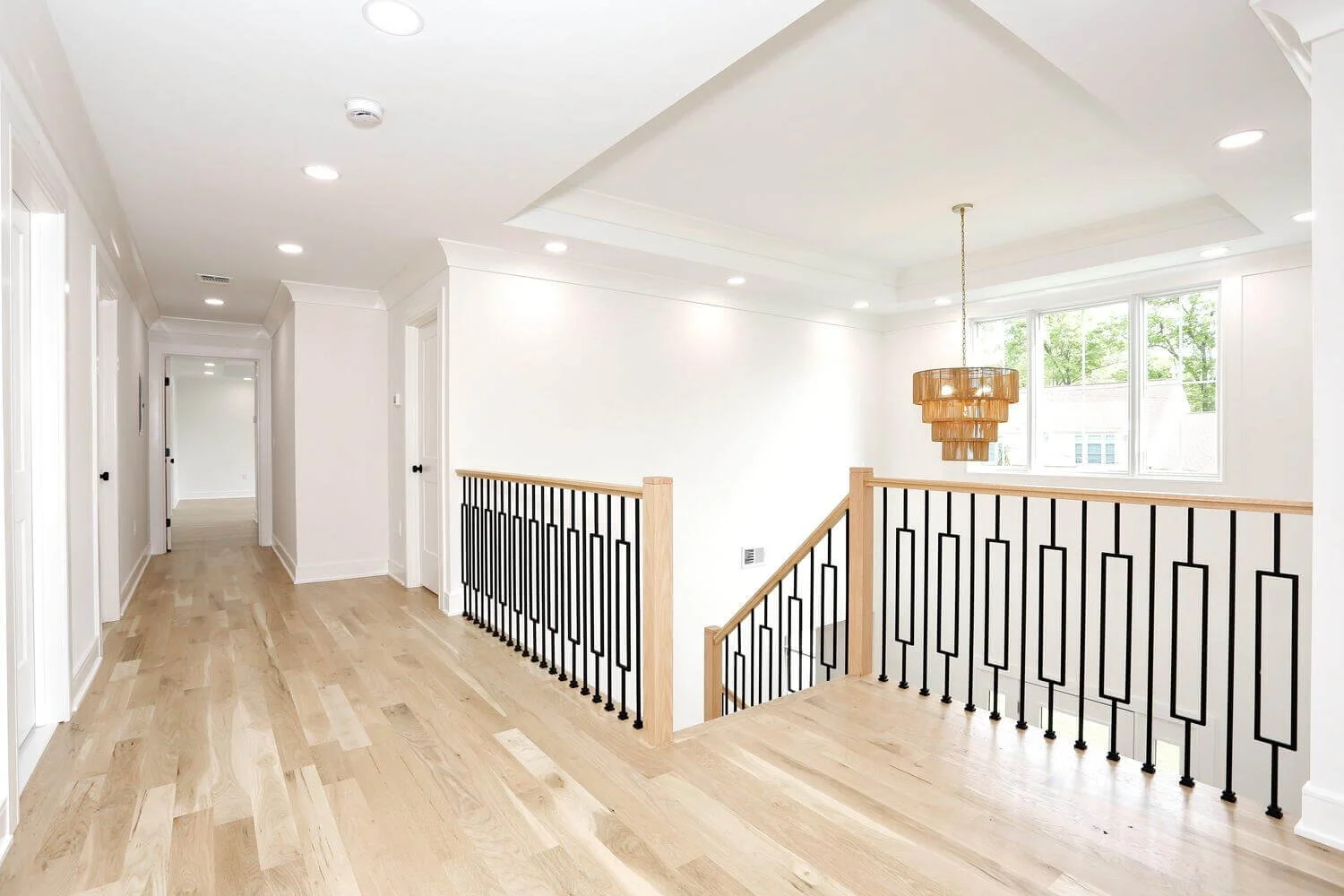 Upstairs landing with modern black metal railing, warm hardwood floors, and natural light in a custom home by DADAK LLC.