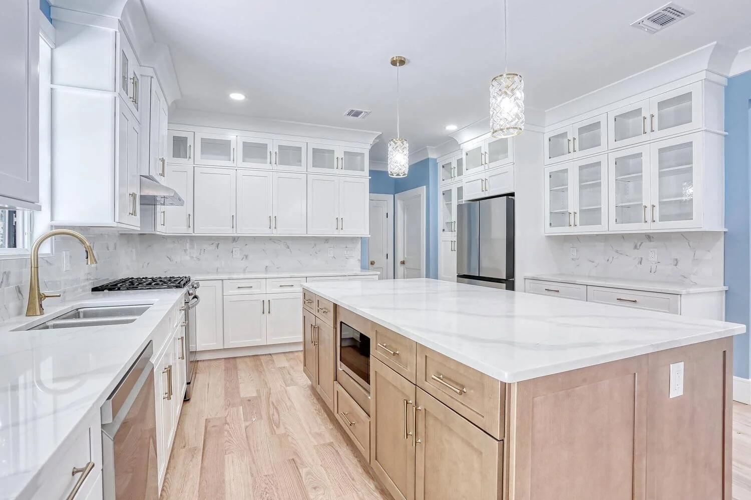Spacious kitchen in a Montvale custom home built by Dadak LLC, featuring white cabinetry, marble-style countertops, pendant lighting, and a large wood island.