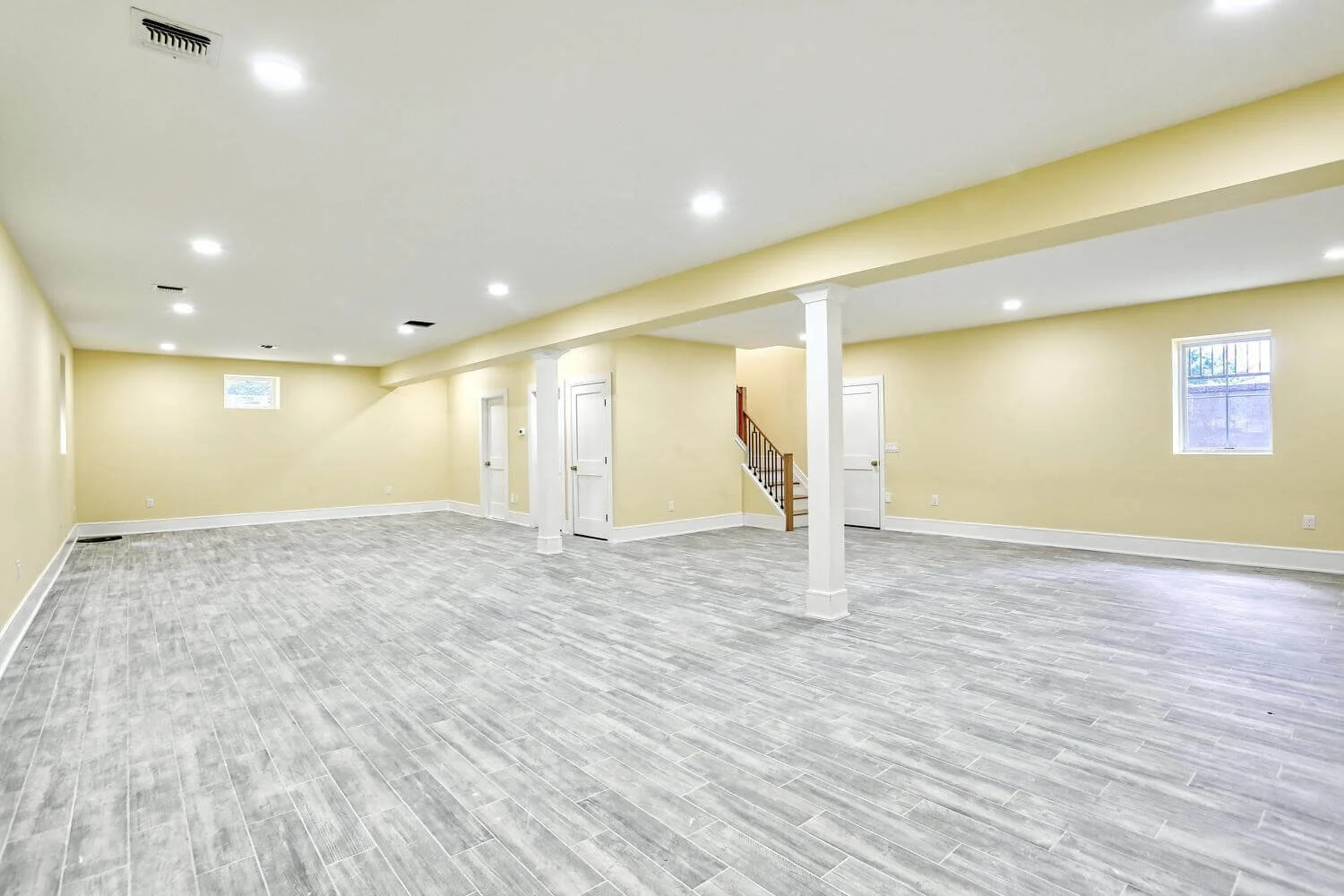 Finished basement with open layout, support columns, and gray tile flooring in Montvale custom home.