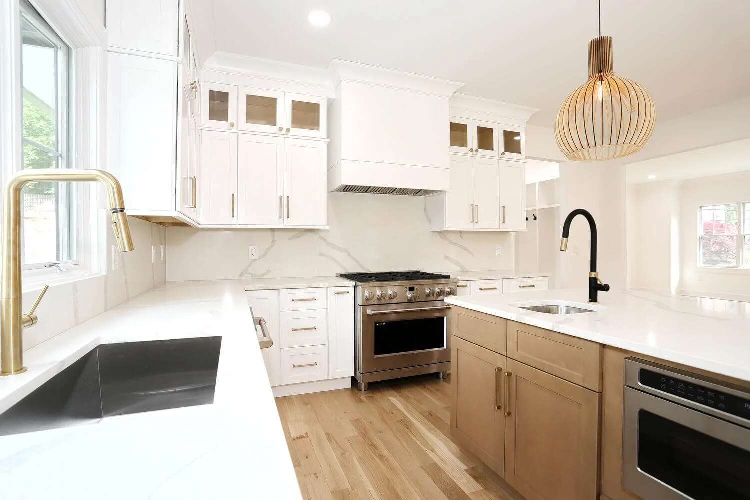 Custom vent hood and white shaker cabinets with brass hardware in a modern farmhouse kitchen by Dadak LLC, Park Ridge, NJ.