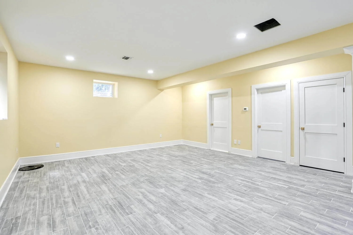 Large basement with multiple doors, yellow walls, and light gray tile flooring in Montvale home.