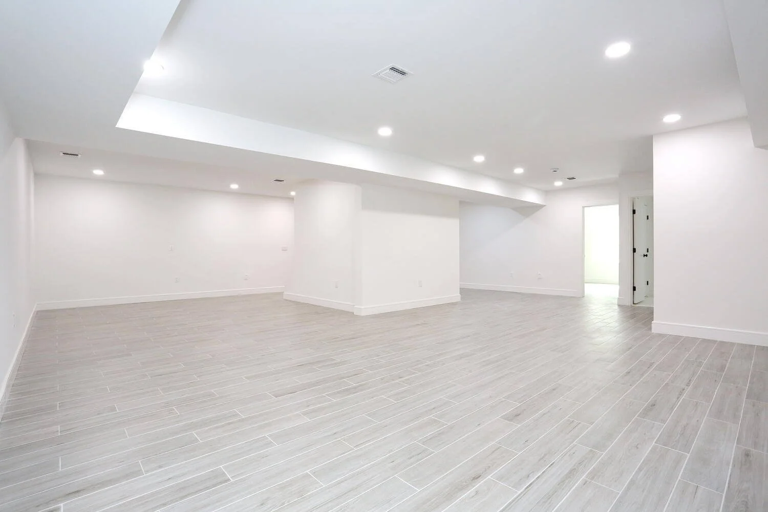 Expansive lower level recreation room with bright recessed lighting and modern neutral finishes in a Park Ridge modern farmhouse by Dadak LLC.