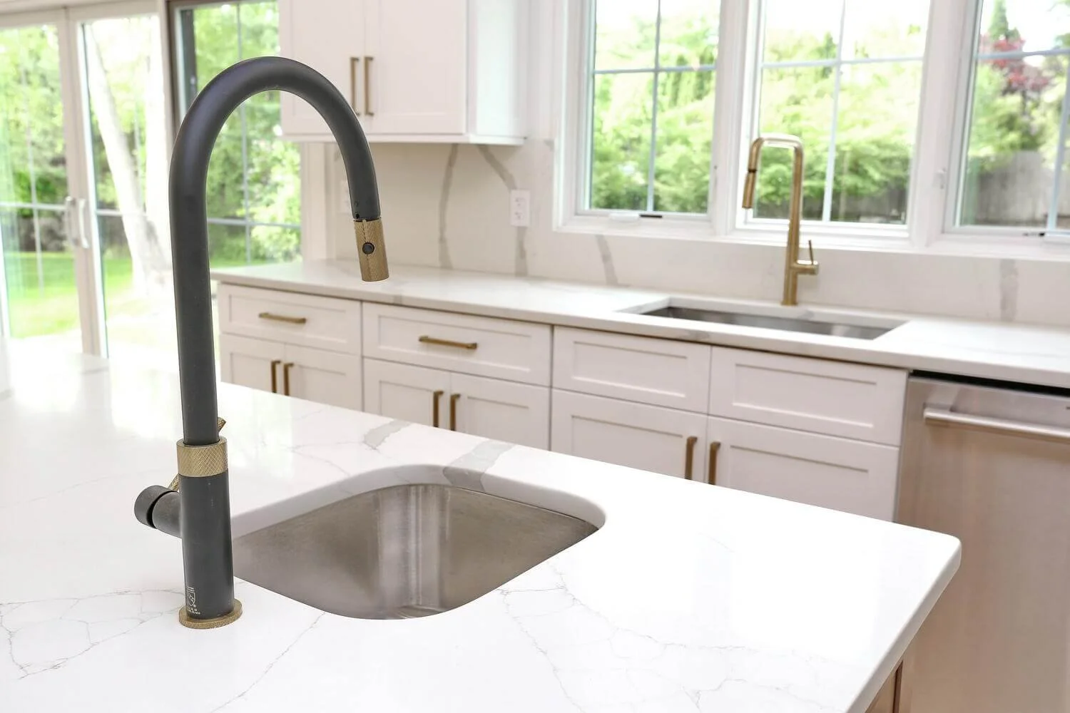 Close-up of black and brass kitchen faucet on quartz island countertop in a modern farmhouse by Dadak LLC, Park Ridge, NJ.