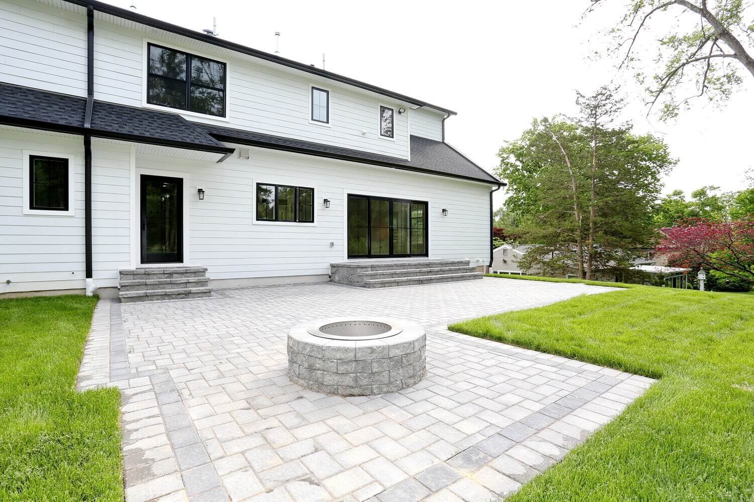 Backyard patio with built-in circular fire pit and gray paver flooring outside a Park Ridge modern farmhouse by Dadak LLC.