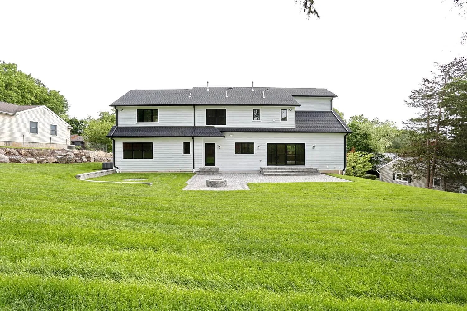 Expansive backyard lawn with fire pit area and patio steps behind a modern farmhouse in Park Ridge by Dadak LLC.