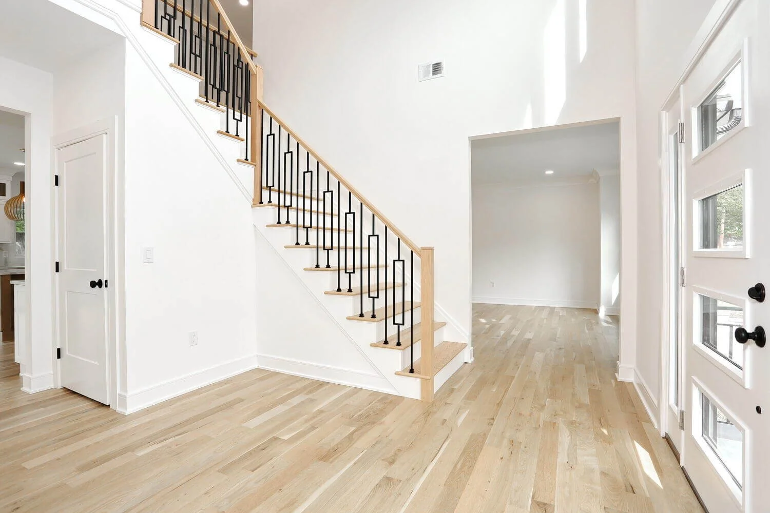 Modern staircase with black metal railings and natural wood treads near the front entryway of a custom home by Dadak LLC, Park Ridge, NJ.