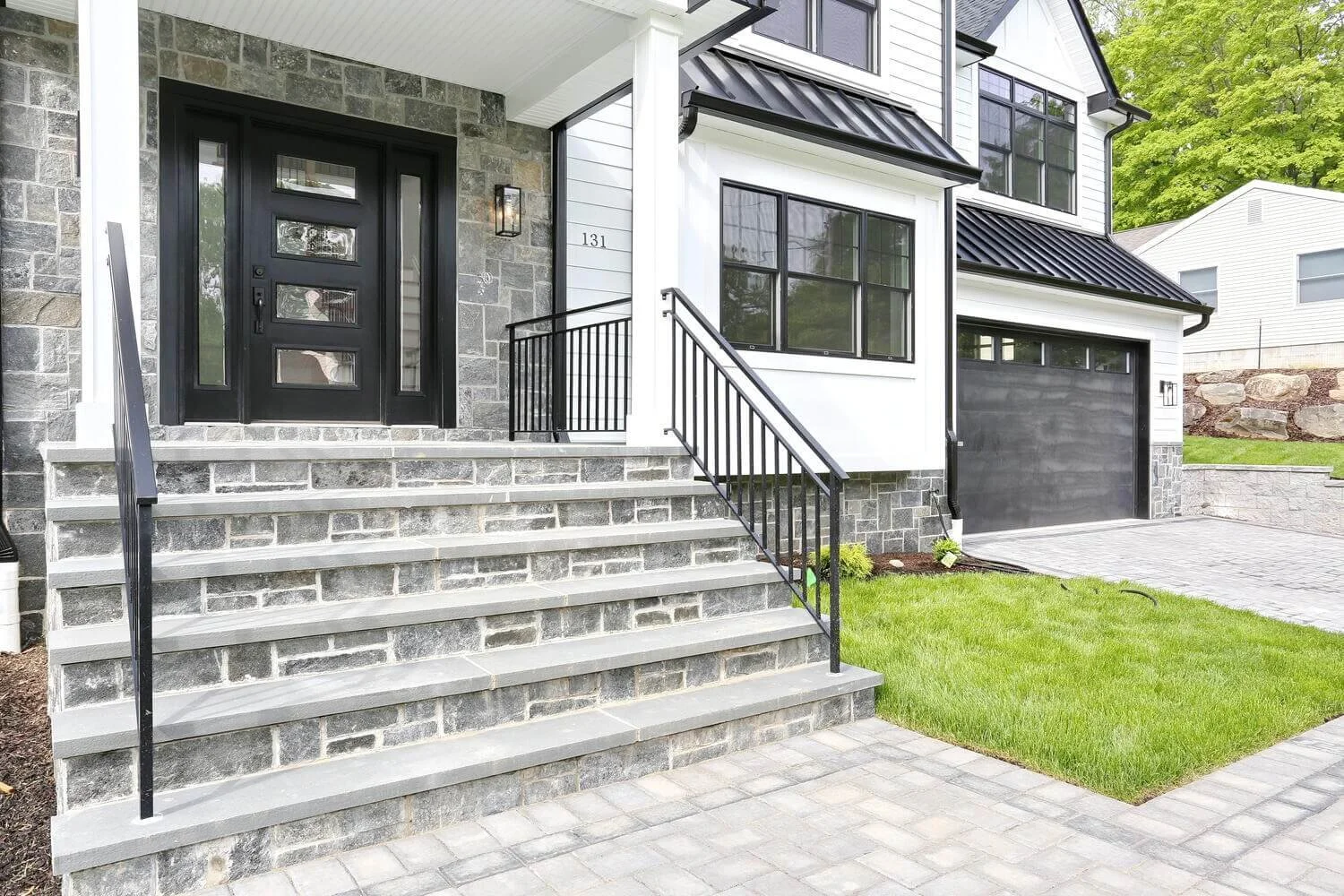 Front entry of a modern farmhouse built by Dadak LLC in Park Ridge, featuring stone steps, black front door, and black metal railings.
