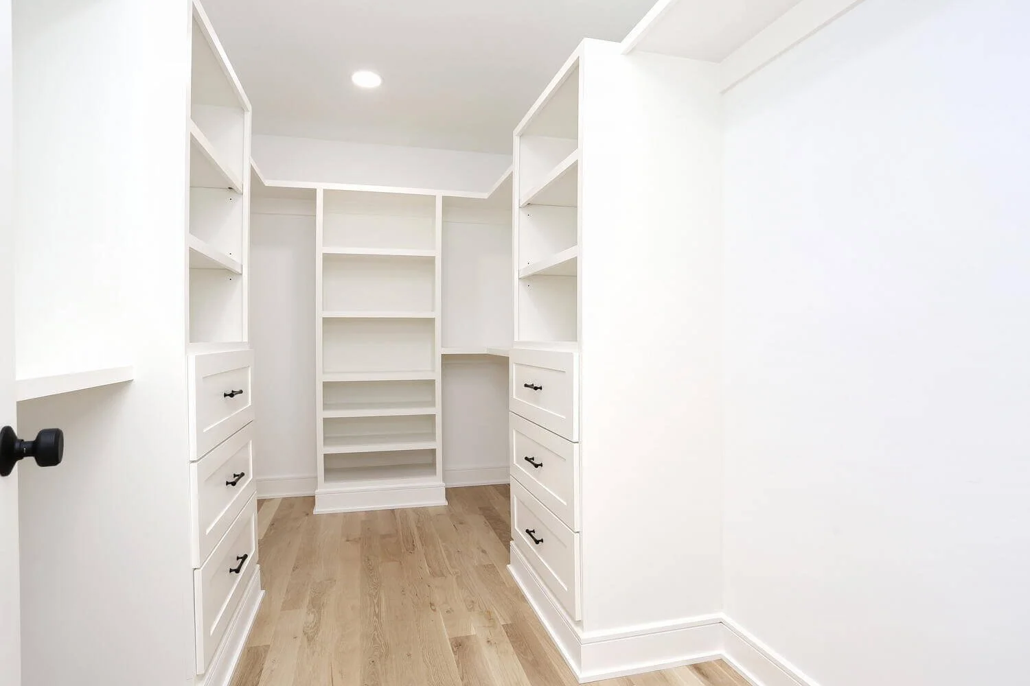 Spacious walk-in primary closet with built-in shelving, drawers, and hardwood floors in a Park Ridge modern farmhouse by Dadak LLC.