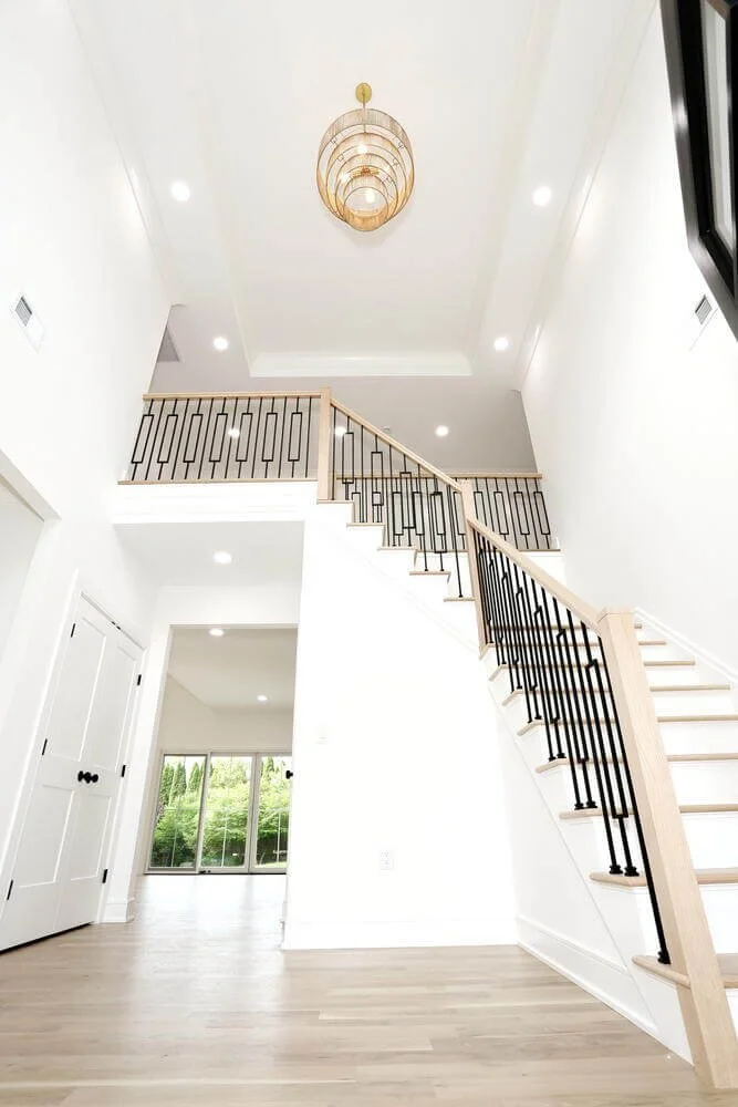 Two-story foyer with gold chandelier and elegant staircase in a modern farmhouse custom build by Dadak LLC, Park Ridge, NJ.