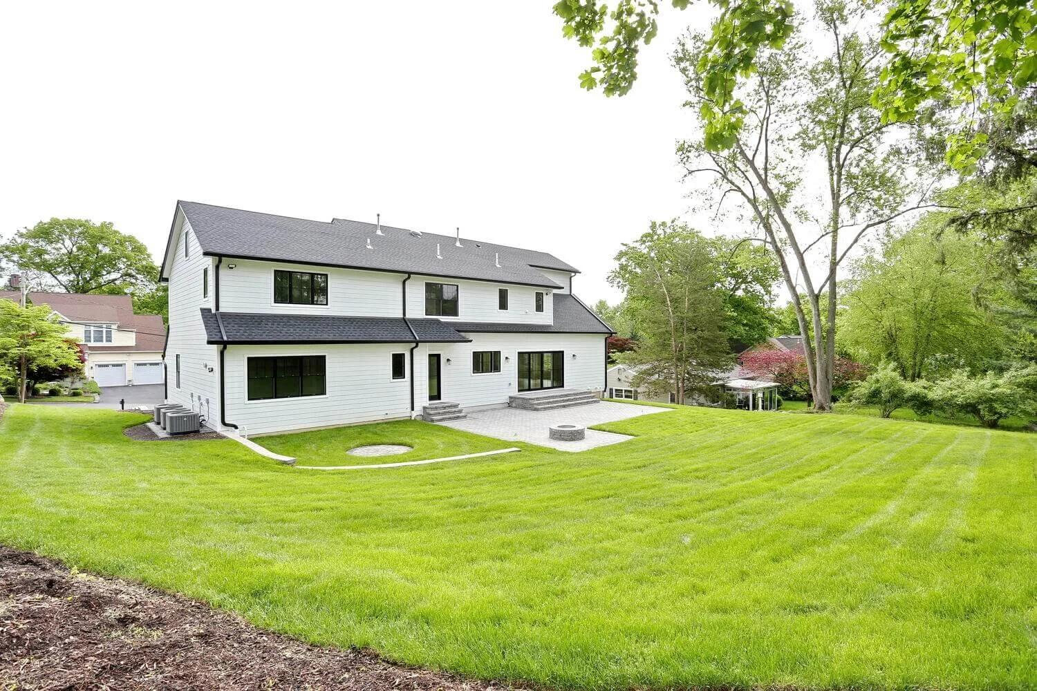 Large backyard with open grass area and stone patio behind a modern farmhouse in Park Ridge by Dadak LLC.