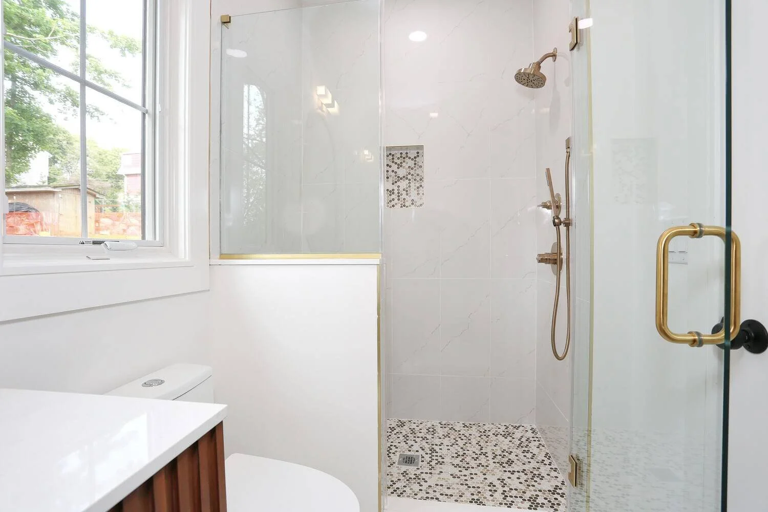 Bright bathroom featuring walk-in shower with mosaic tile floor and gold fixtures in a Park Ridge modern farmhouse by Dadak LLC.