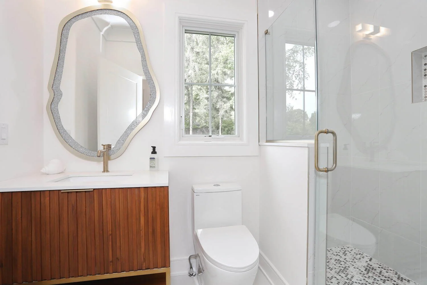 Modern bathroom with wood vanity, unique mirror, and glass shower enclosure in a Park Ridge modern farmhouse by Dadak LLC.