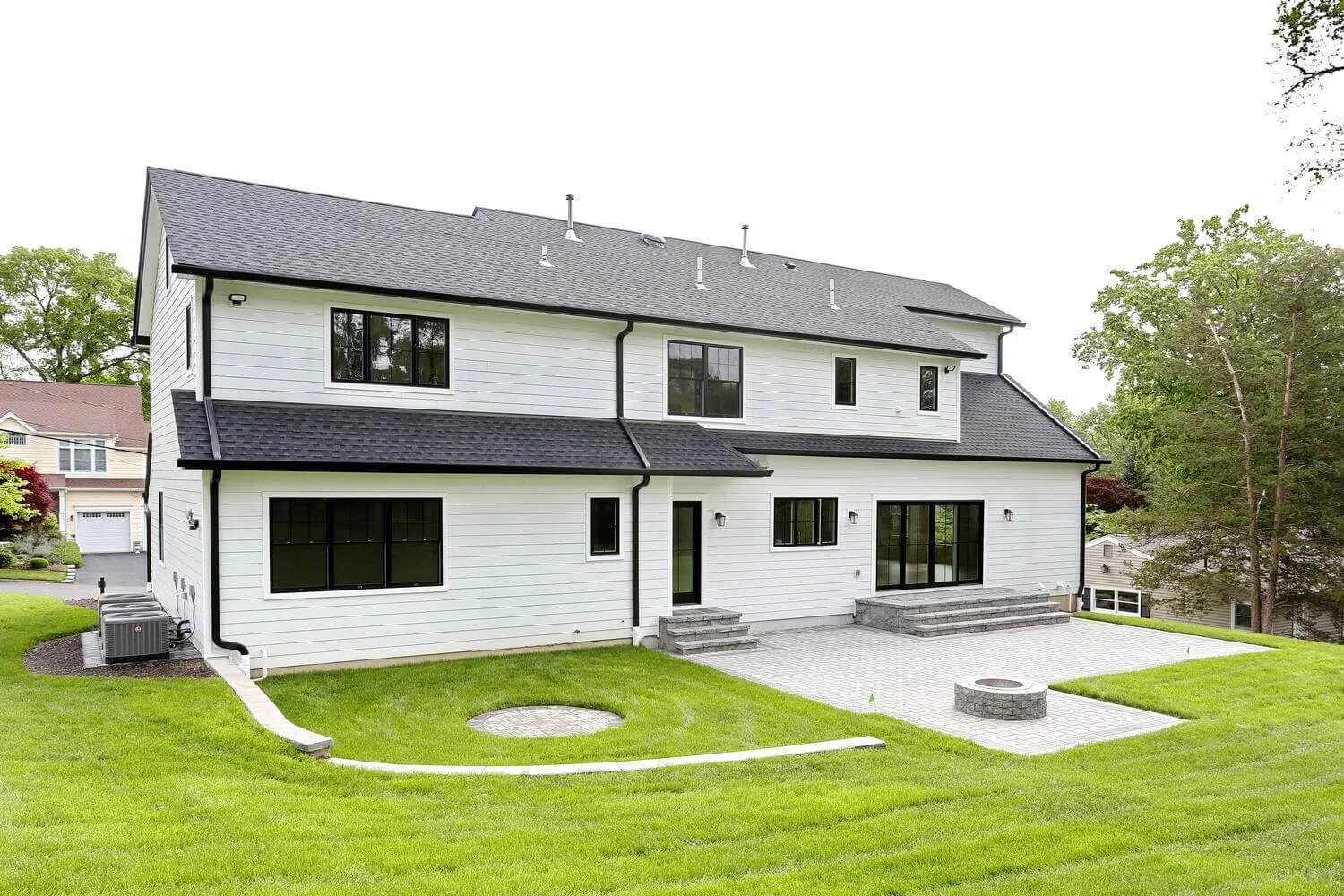 Full rear view of the modern farmhouse with black windows, white siding, and landscaped backyard lawn in Park Ridge by Dadak LLC.