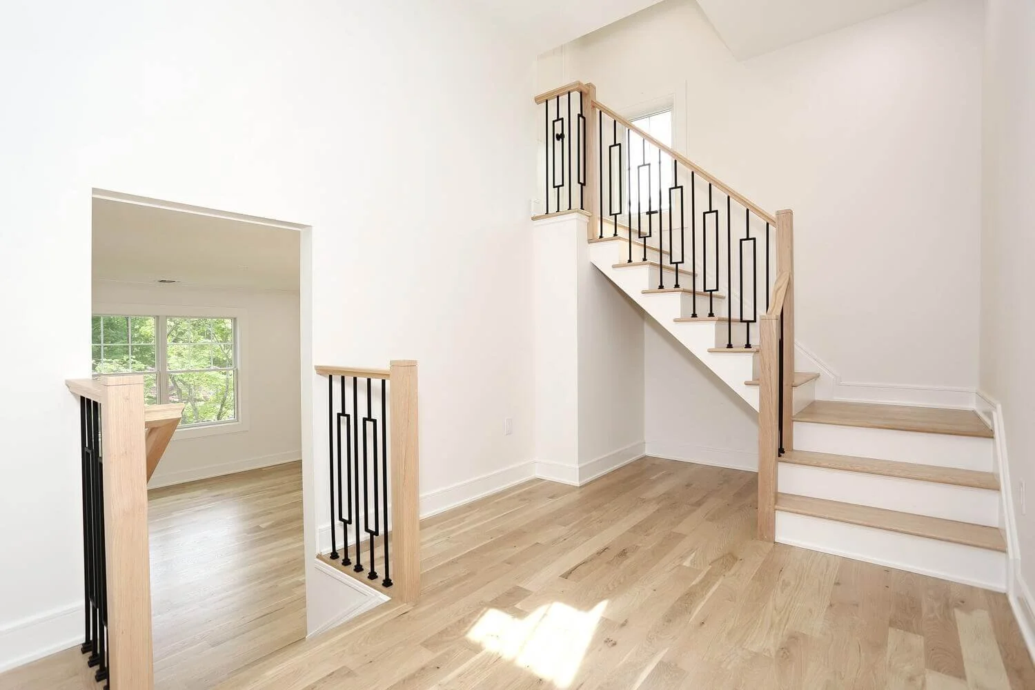 Hallway with modern staircase featuring black iron railings and light oak wood accents in a Park Ridge modern farmhouse by Dadak LLC.
